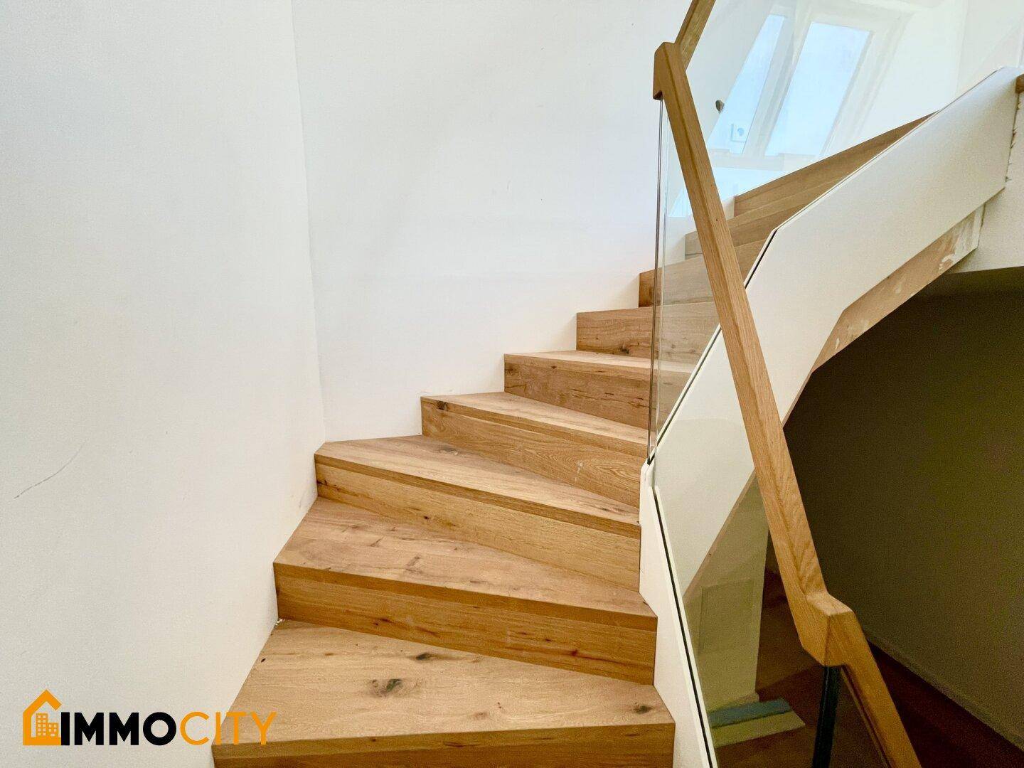 Moderne Holztreppe mit Glasgeländer und viel natürlichem Licht im Treppenhaus.