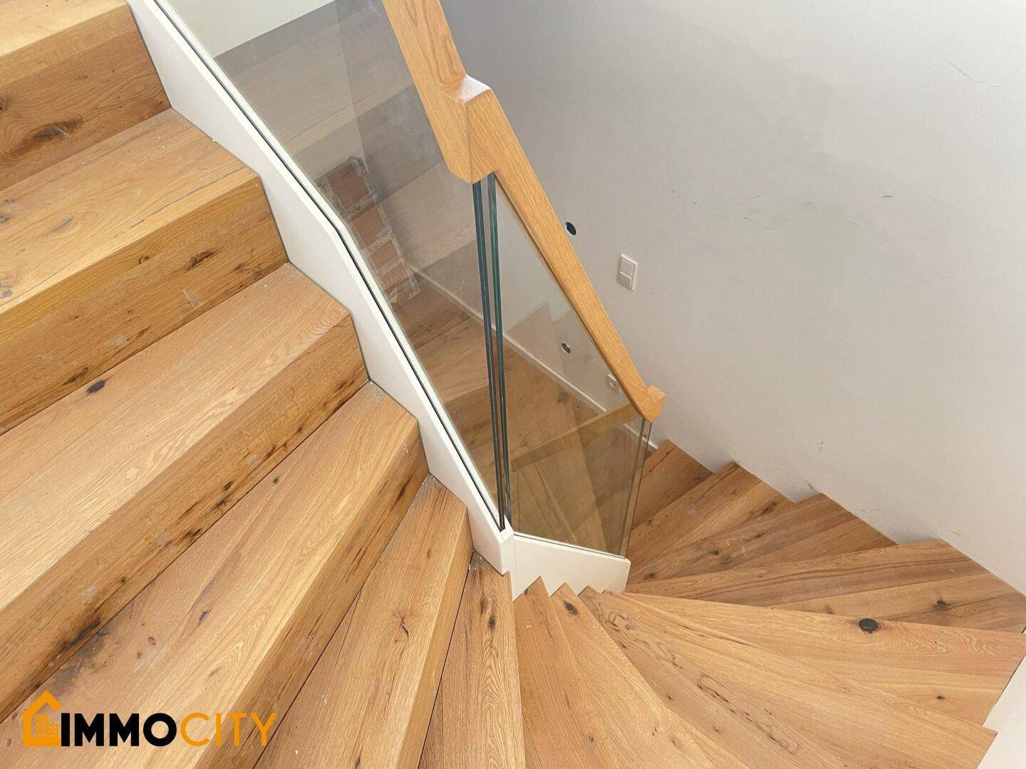 Elegante Holztreppe mit modernem Glasgeländer, die die Etagen verbindet.