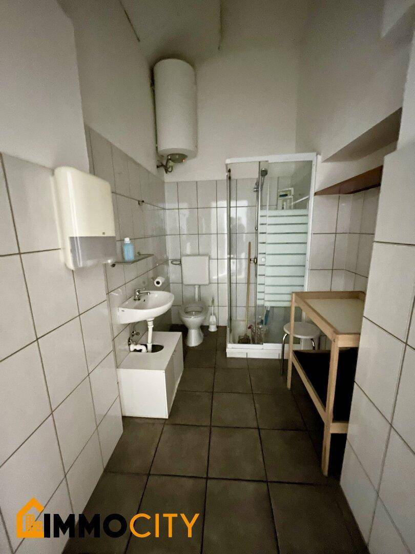 Badezimmer mit Dusche, WC, Waschbecken und weißen Fliesen an den Wänden.