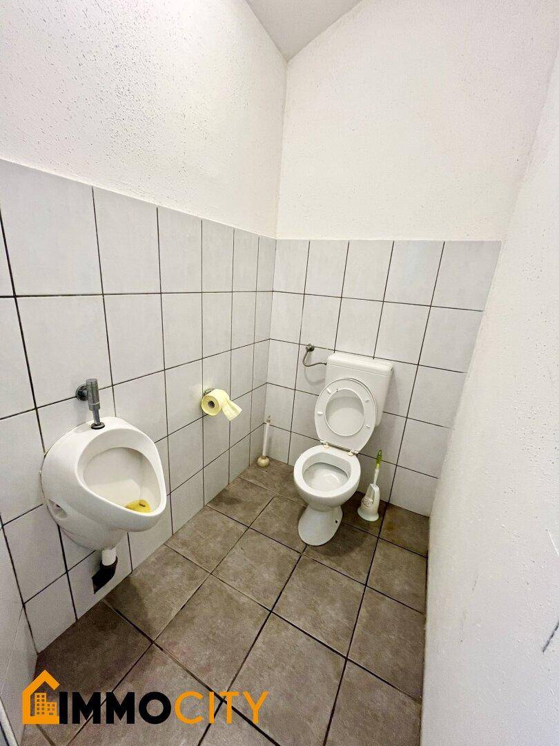 Toilettenraum mit WC und Urinal, ausgestattet mit weißen Wandfliesen.