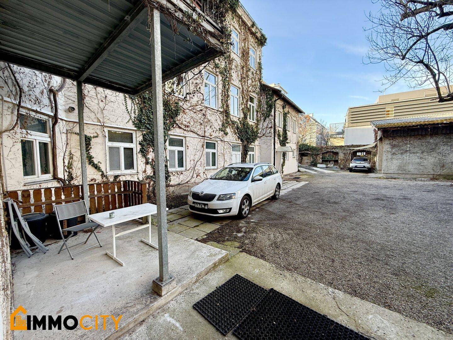 Überdachte Terrasse mit einfacher Sitzgelegenheit und Blick auf den Innenhof.