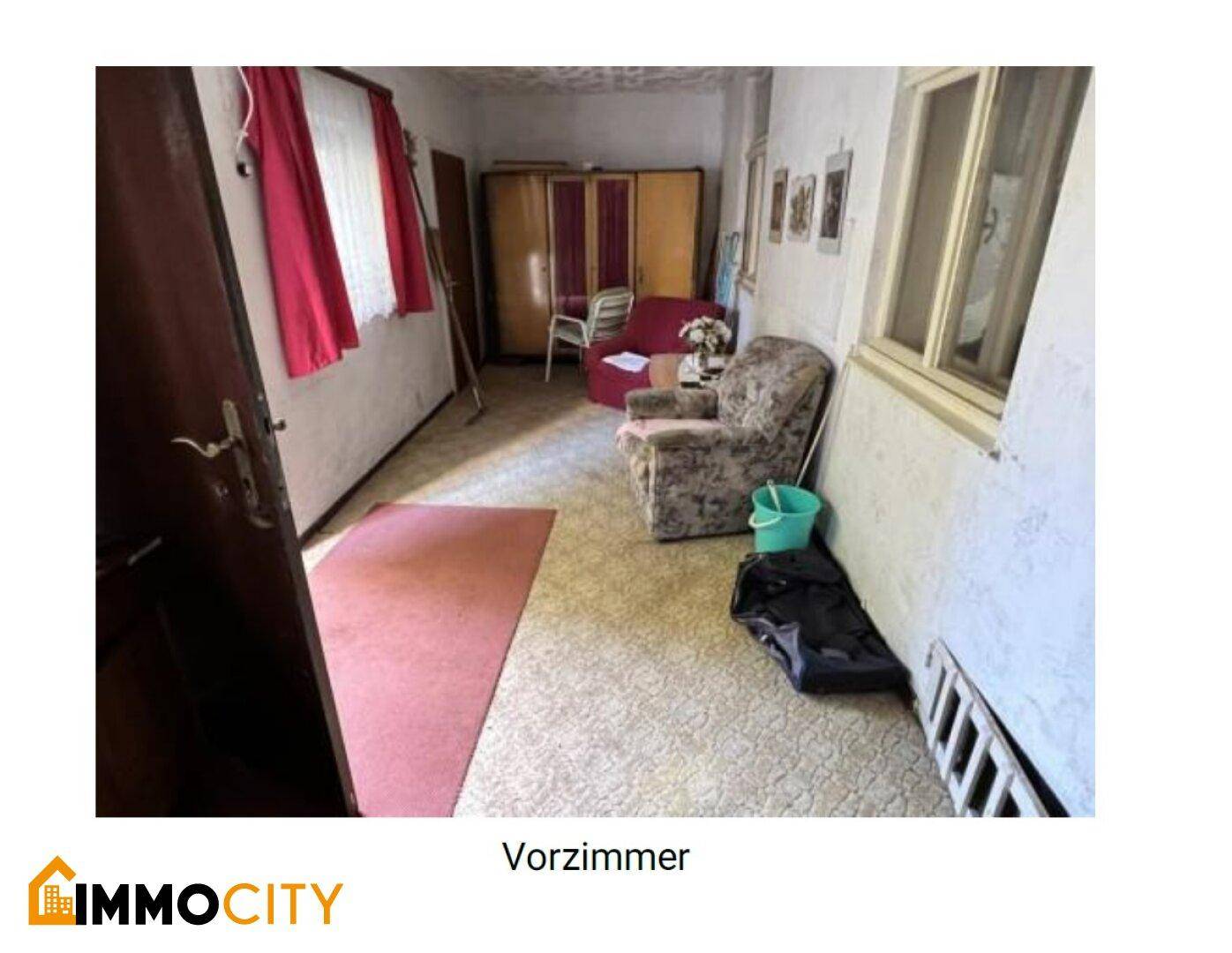 Vorzimmer mit Teppichboden, älteren Möbeln und einem Fenster, das Tageslicht hereinlässt.