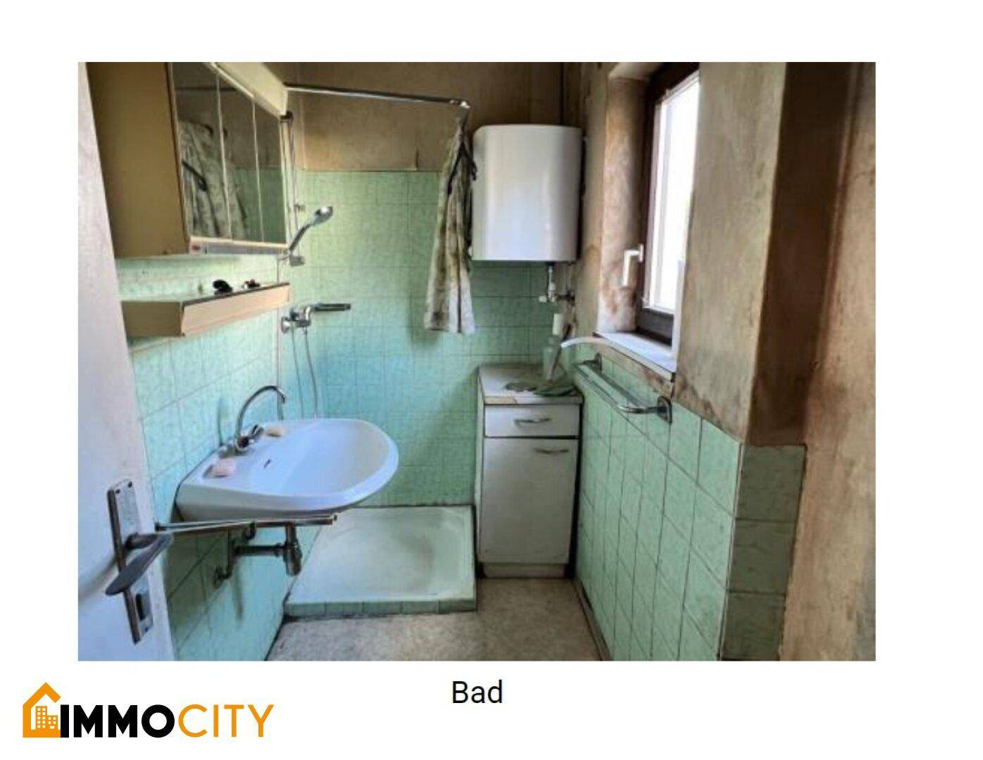 Badezimmer mit grünen Fliesen, Waschbecken, Spiegelschrank und einem Fenster für Belüftung.
