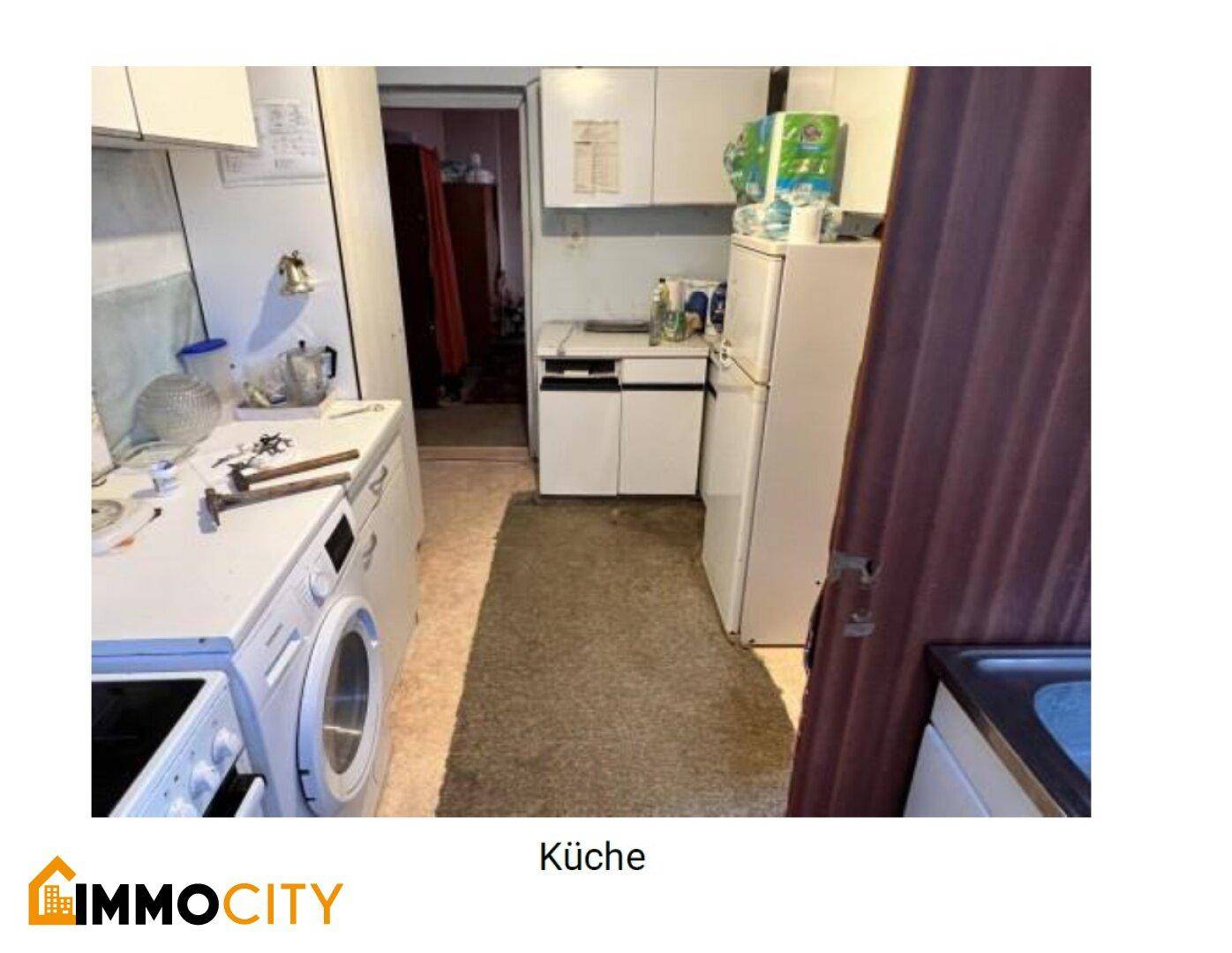 Küche mit älteren Einbauschränken, Kühlschrank und Waschmaschine, die eine Modernisierung benötigt.