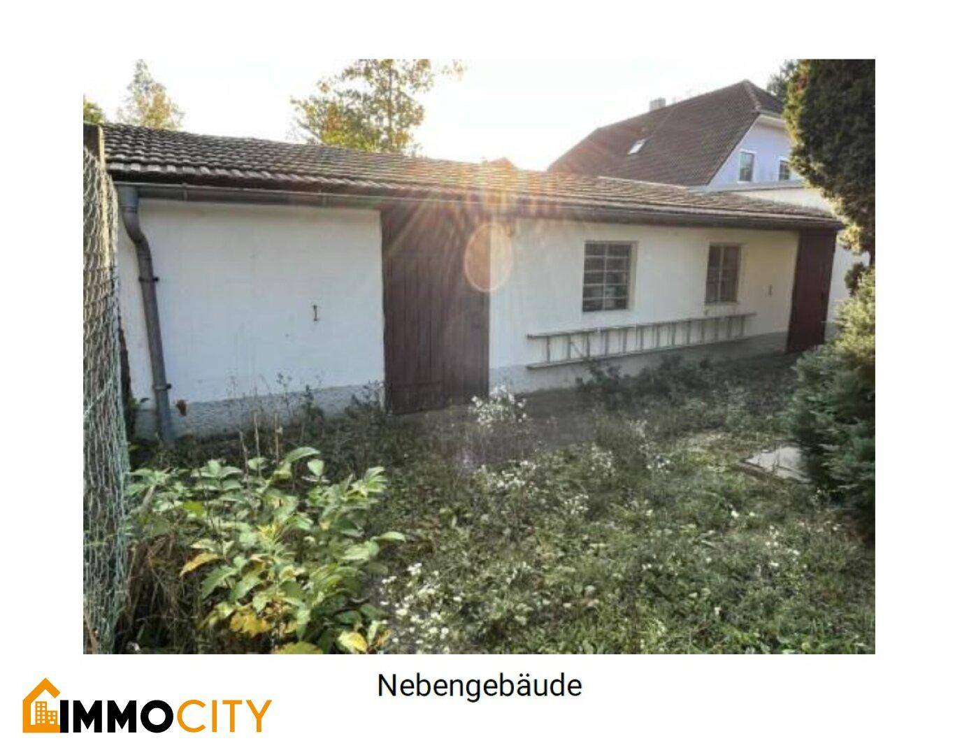 Nebengebäude mit Fenstern und einem großen Holztor, das als Garage oder Werkstatt dienen könnte.