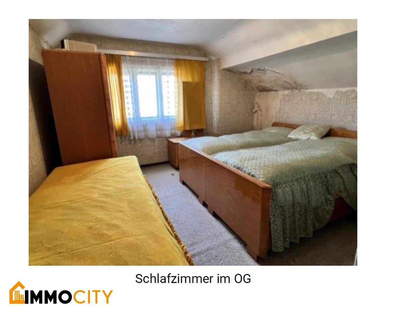 Schlafzimmer im Obergeschoss mit zwei Betten, Holzschrank und einer Dachschräge.