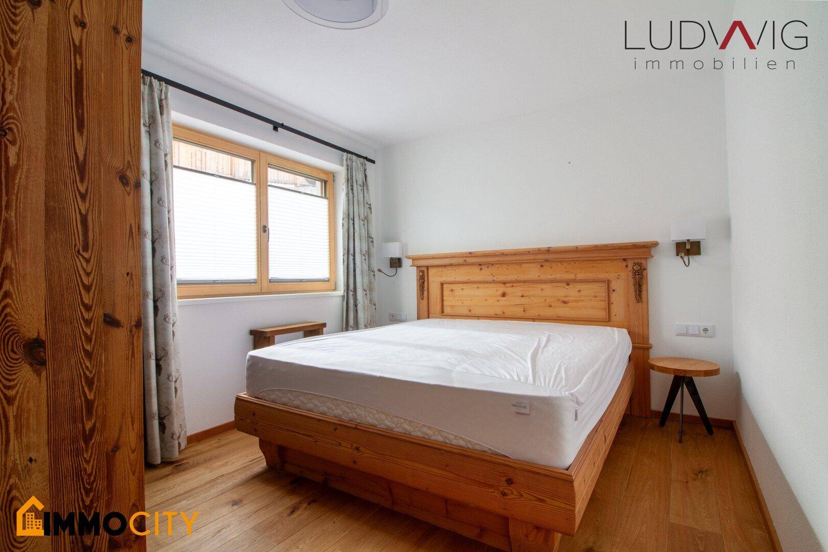 Gemütliches Schlafzimmer mit Holzbett, Holzboden und Fenster mit Blick ins Grüne.
