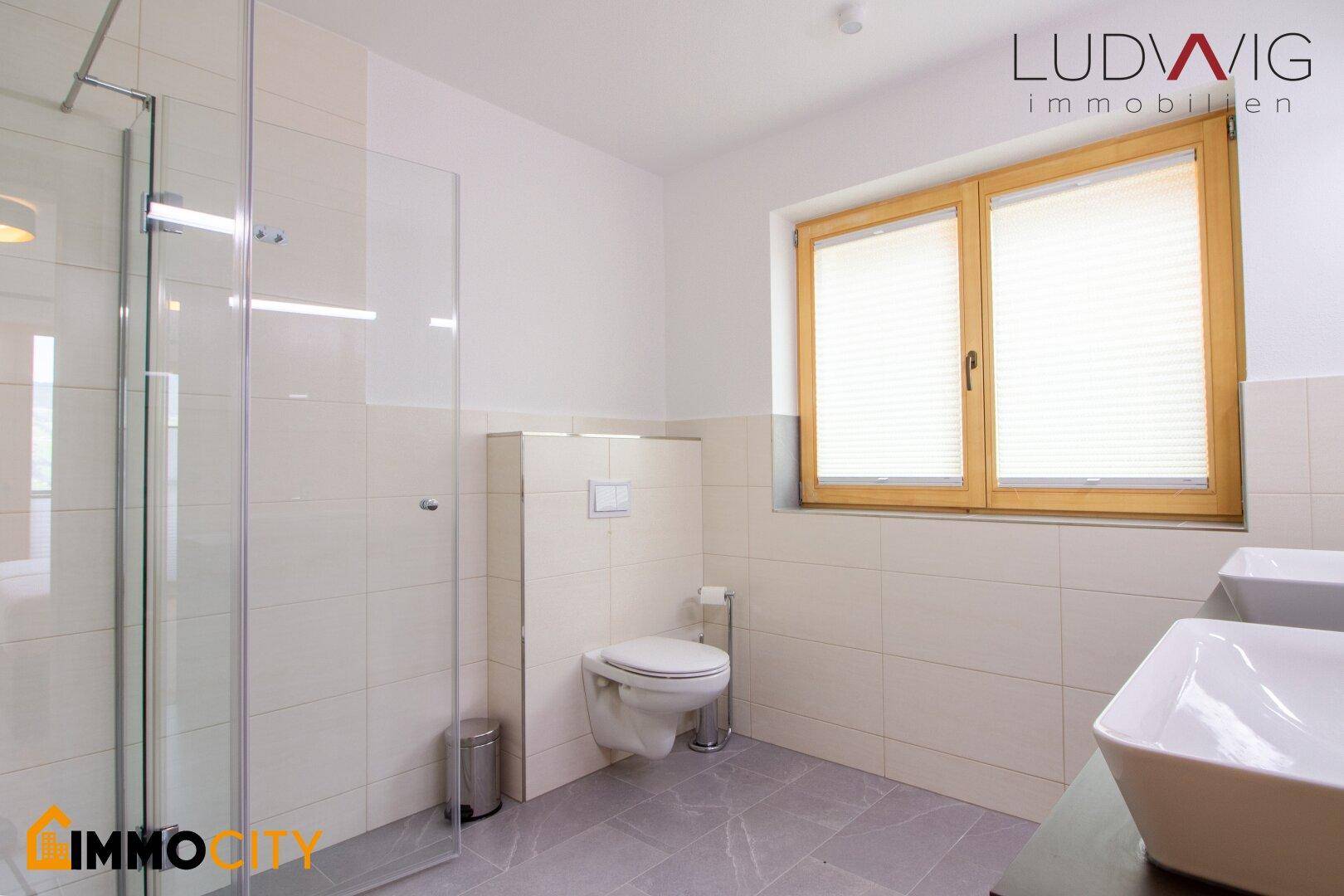 Helles Badezimmer mit großer Glasdusche, Wand-WC und zwei Aufsatzwaschbecken.