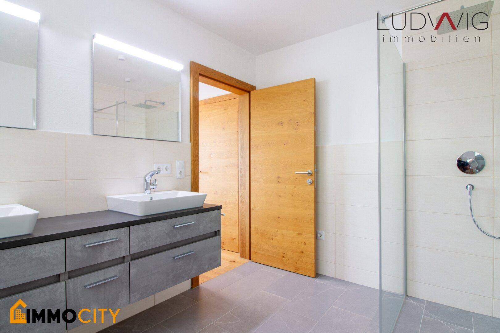 Modernes Badezimmer mit Doppelwaschtisch, großer Dusche und Holztüren.