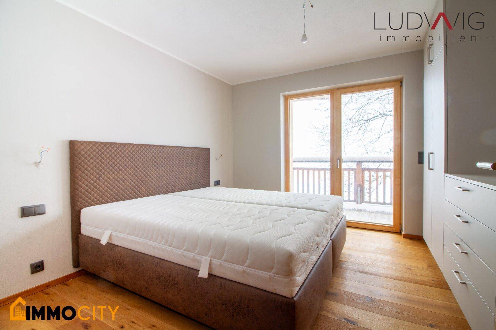Schlafzimmer mit Doppelbett, Holzboden und direktem Zugang zum Balkon.