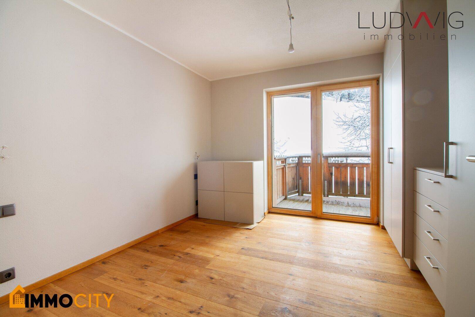 Helles Schlafzimmer mit Holzboden und großem Fenster mit Balkonzugang.