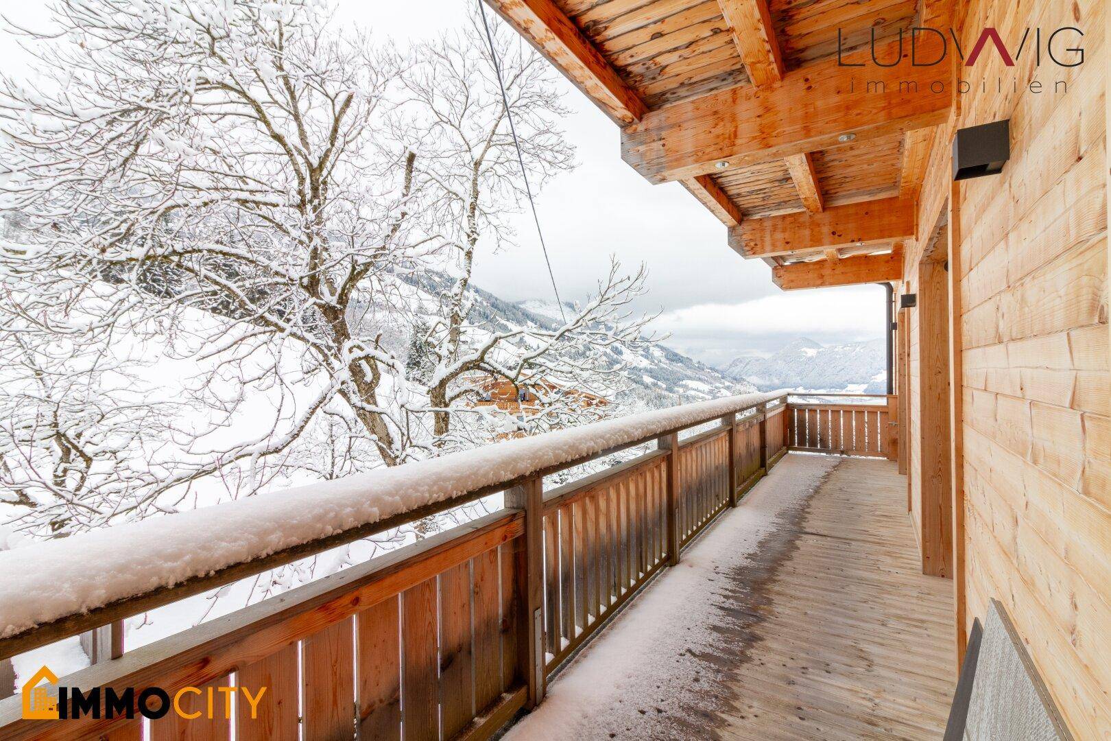 Langer Holzbalkon mit Schnee und weitem Blick auf die verschneite Winterlandschaft.