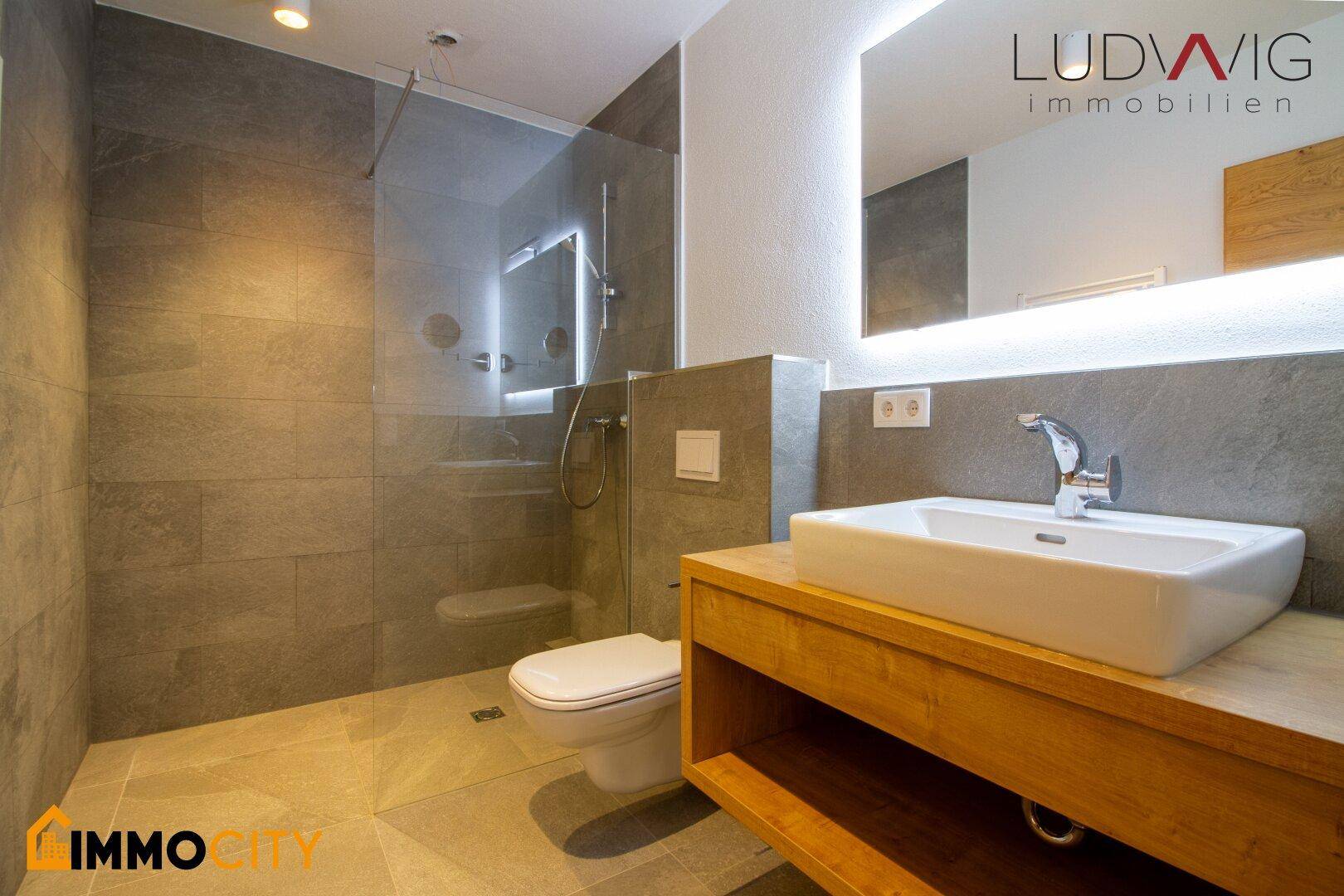 Modernes Badezimmer mit begehbarer Dusche, Wand-WC und eleganten grauen Fliesen.