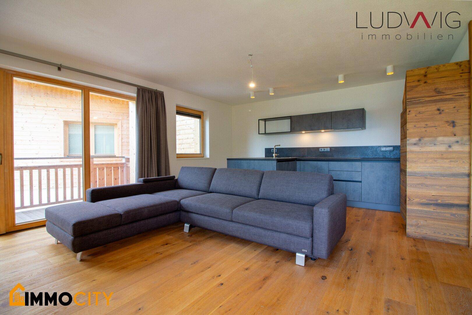 Geräumiger Wohnbereich mit großem Ecksofa, Holzboden und offener Küche.