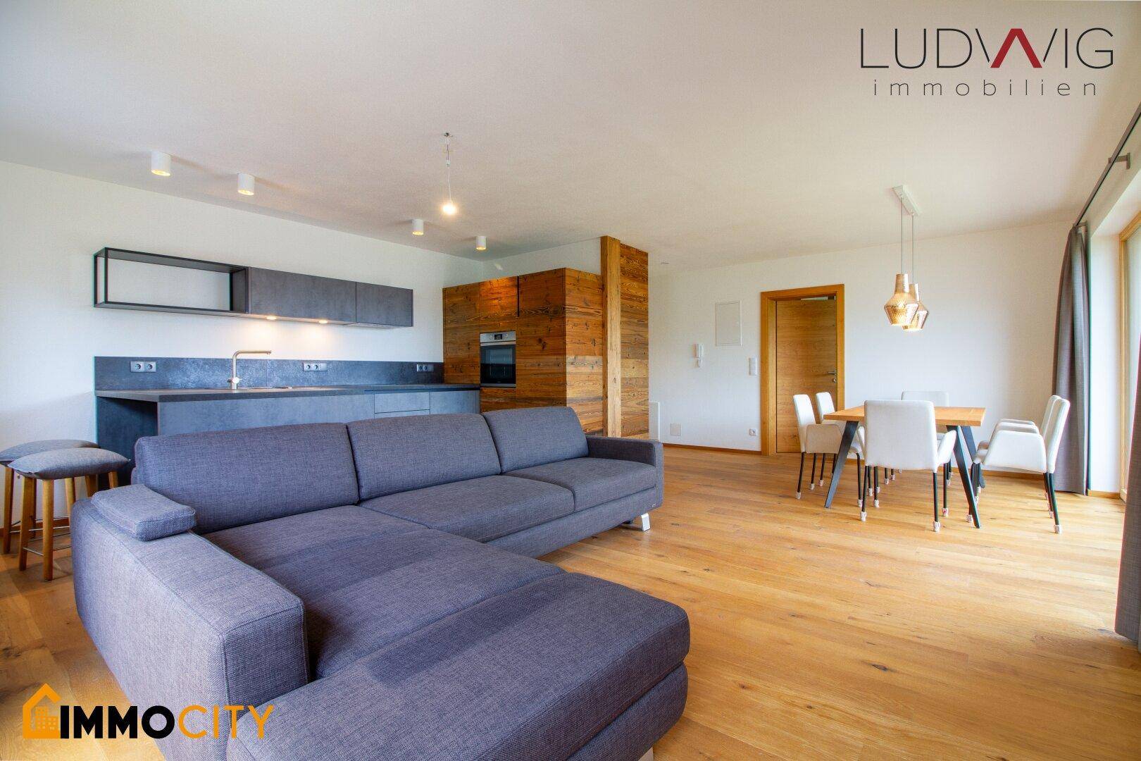 Offener Wohnbereich mit großem Sofa, Holzboden und integrierter moderner Küche.