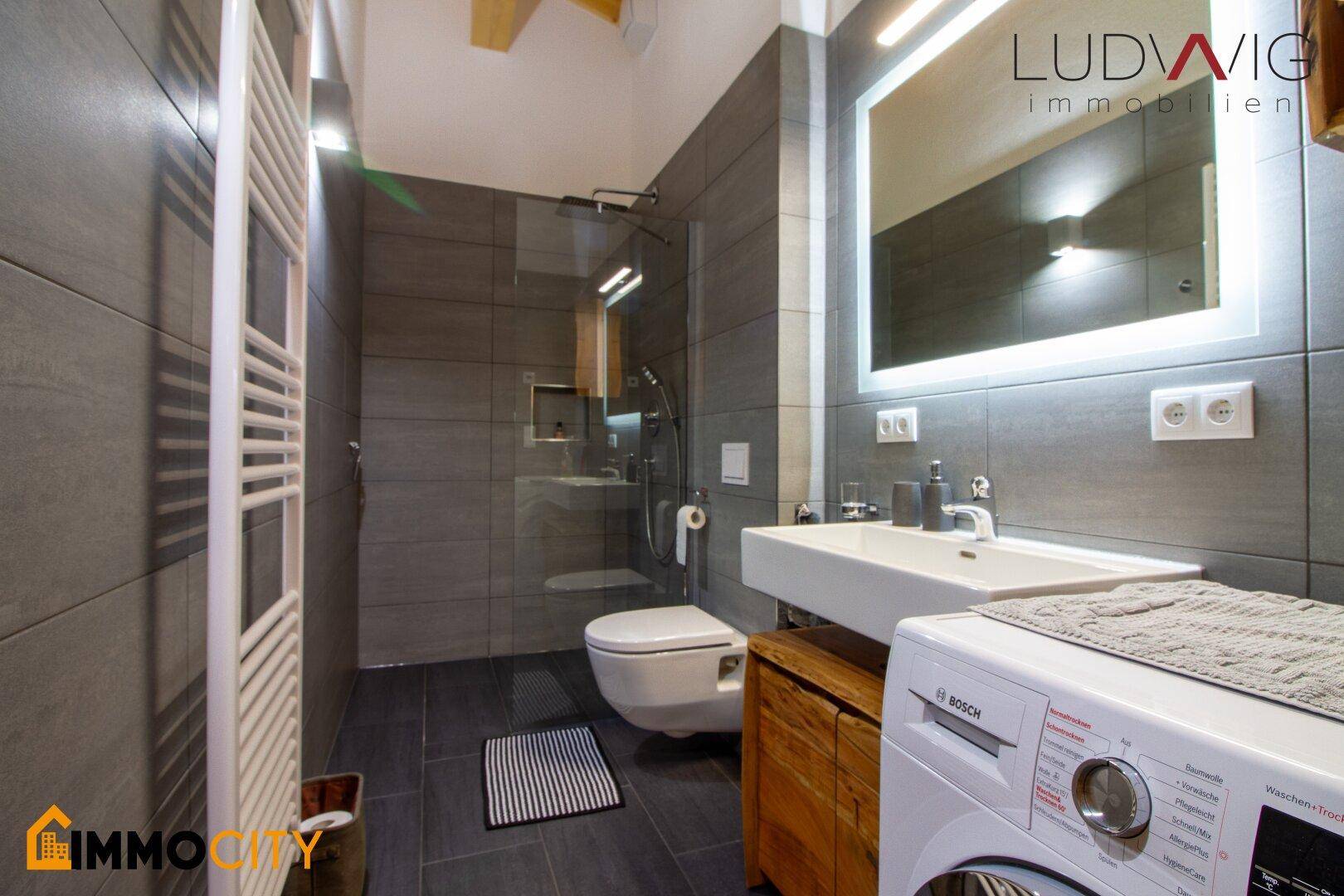 Modernes Badezimmer mit ebenerdiger Dusche, Waschmaschine und beheiztem Handtuchhalter.