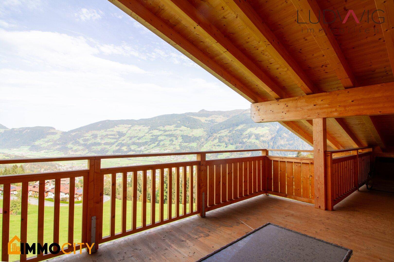 Großer Holzbalkon mit weitem Blick auf die umliegende Berglandschaft und grüne Täler.