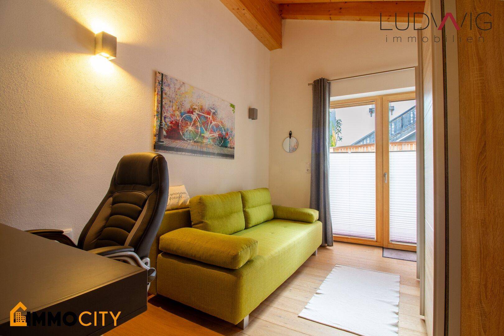 Helles Zimmer mit Schreibtisch, Sofa und Zugang zu einem französischen Balkon.