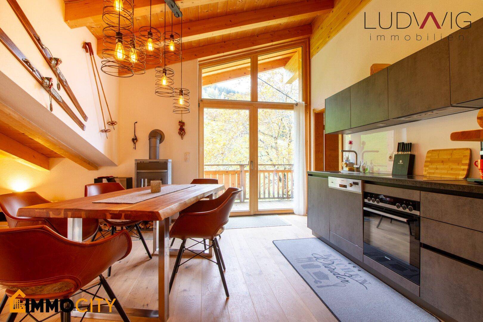 Offener Wohn-Essbereich mit moderner Küche, Kaminofen und Zugang zum Balkon.