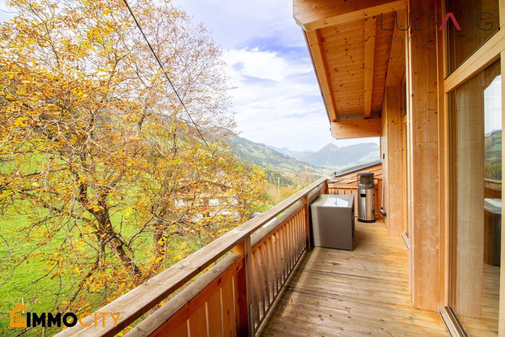 Schmaler Holzbalkon mit Blick auf die herbstliche Natur und die umliegenden Berge.