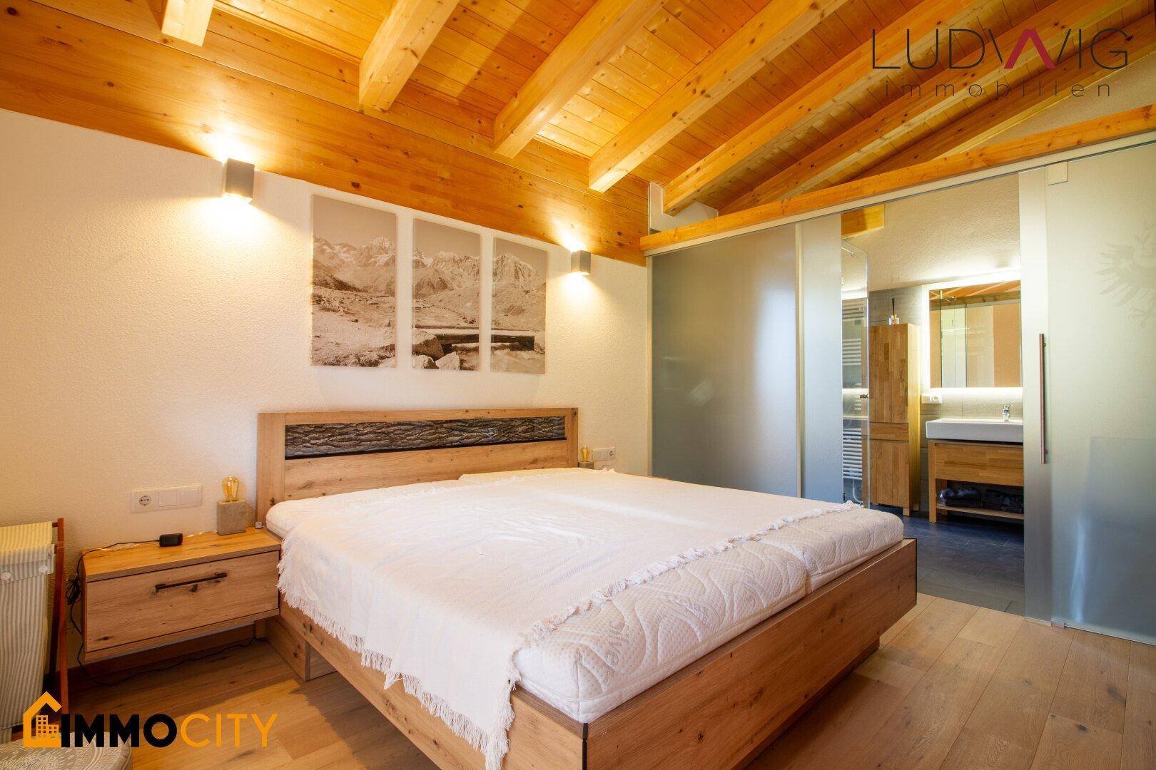 Gemütliches Schlafzimmer mit Holzbett, Nachttischen und Zugang zum Badezimmer.