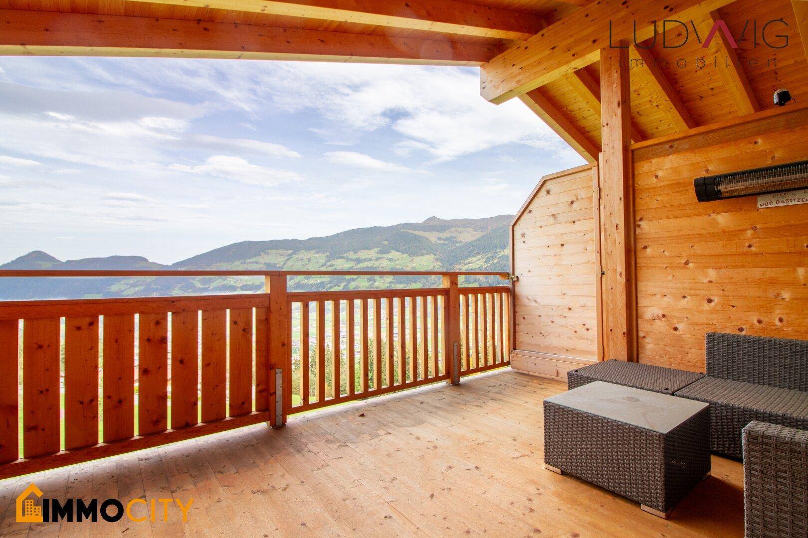 Geräumiger Holzbalkon mit Sitzgelegenheiten und weitem Bergblick.