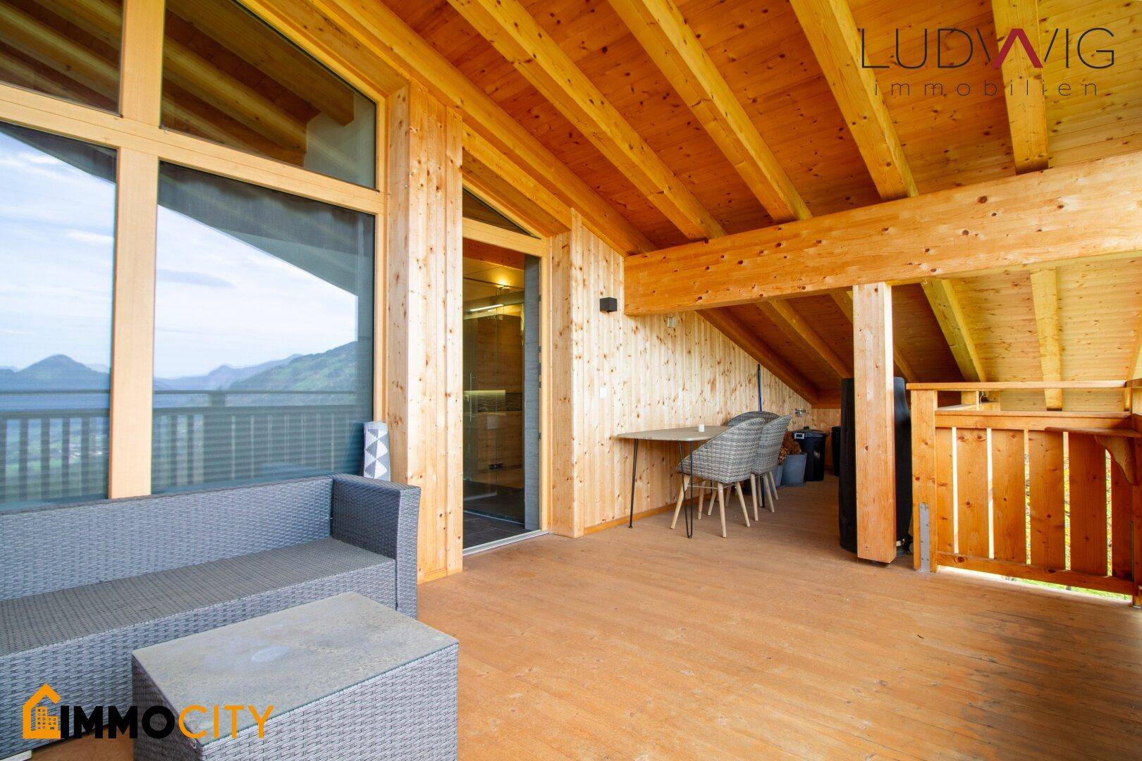 Großer Holzbalkon mit Sitzgelegenheiten und Panoramablick auf die Berge.