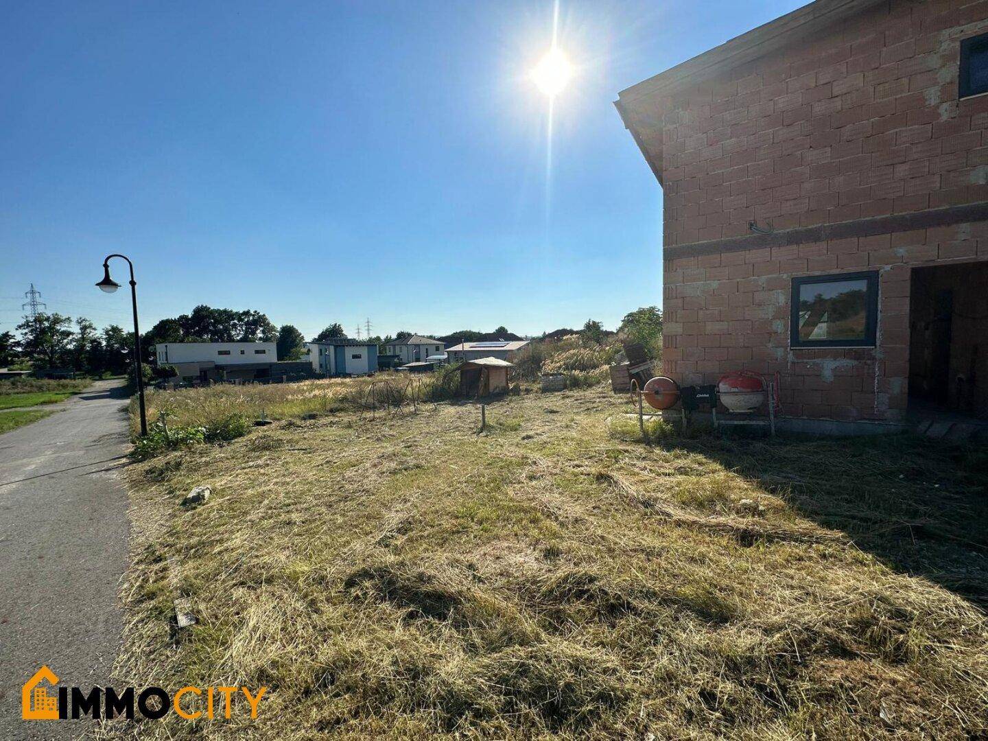 Rohbau eines Hauses mit Ziegelwänden und sonnigem Wetter, umgeben von einem großen Grundstück.