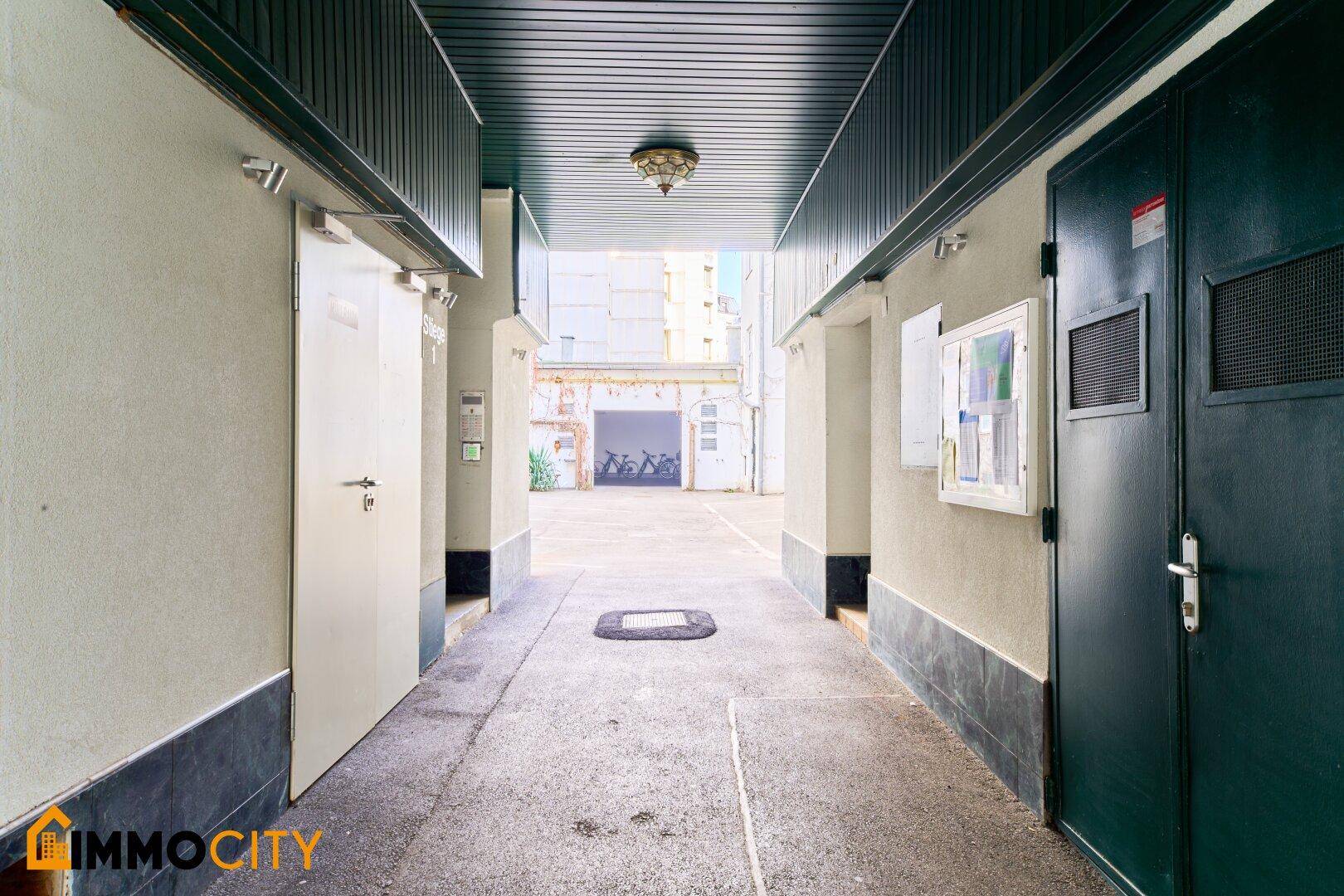 Durchgang zu einem Innenhof mit Blick auf eine Garage im Hintergrund.