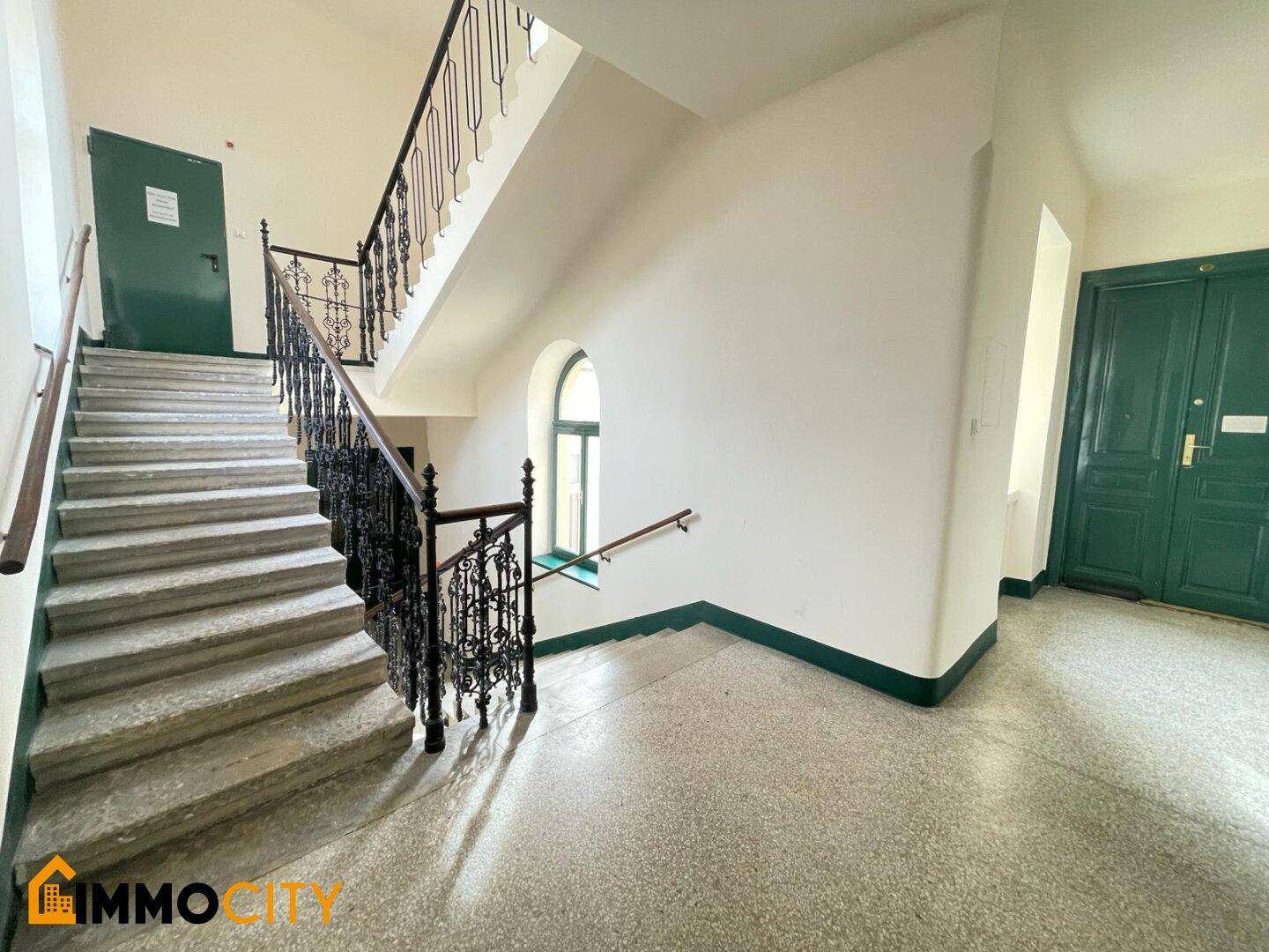 Historisches Treppenhaus mit schmiedeeisernem Geländer, Steinstufen und Fliesenboden, führt zu den oberen Etagen.
