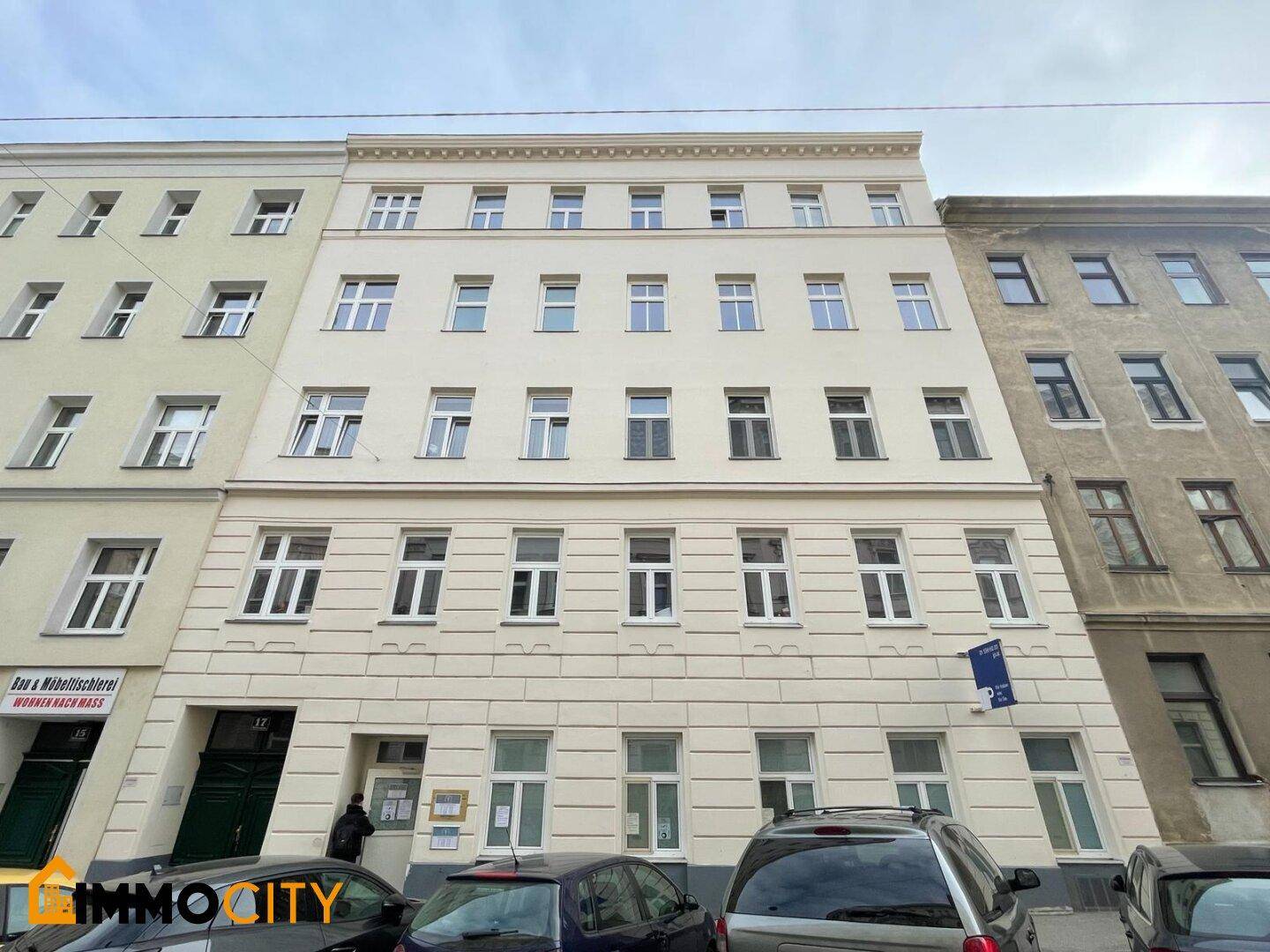 Klassische Fassade eines Mehrfamilienhauses mit vielen Fenstern und geparkten Autos davor.