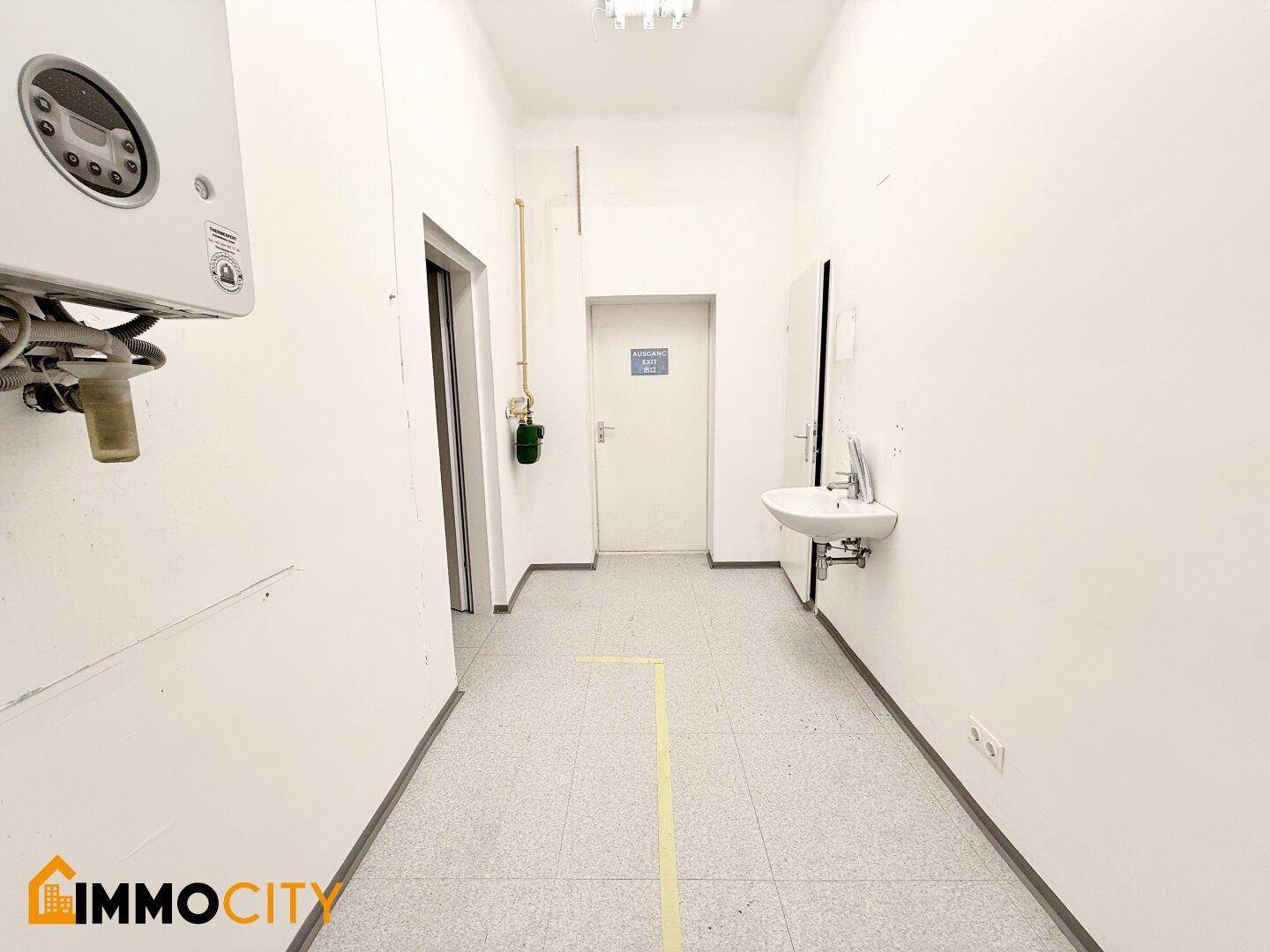 Langer Flur mit Waschbecken, Heiztherme und Fliesenboden, führt zu weiteren Räumen.