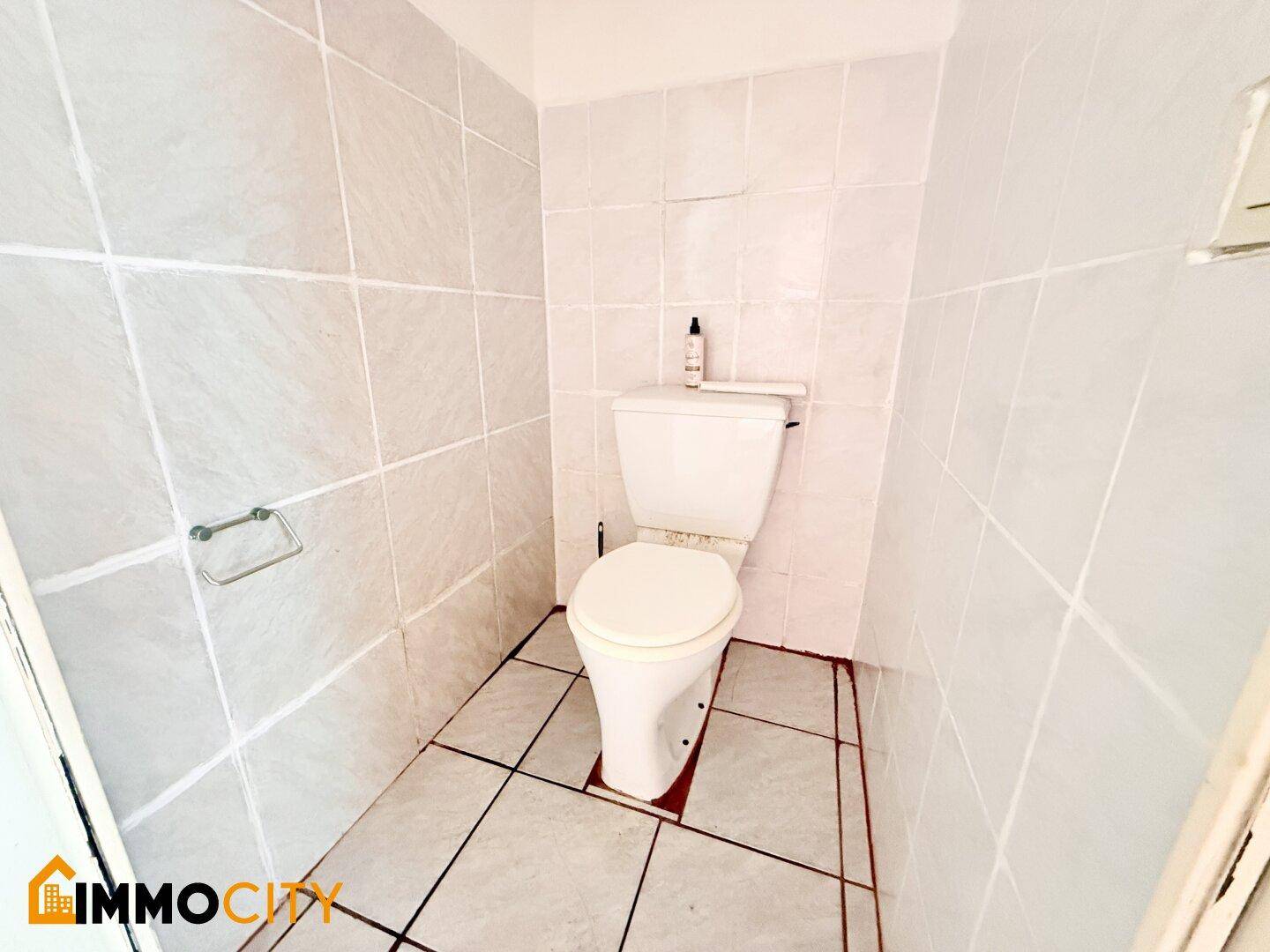 Kleines WC mit weißen Wand- und Bodenfliesen, ausgestattet mit einer Standardtoilette.