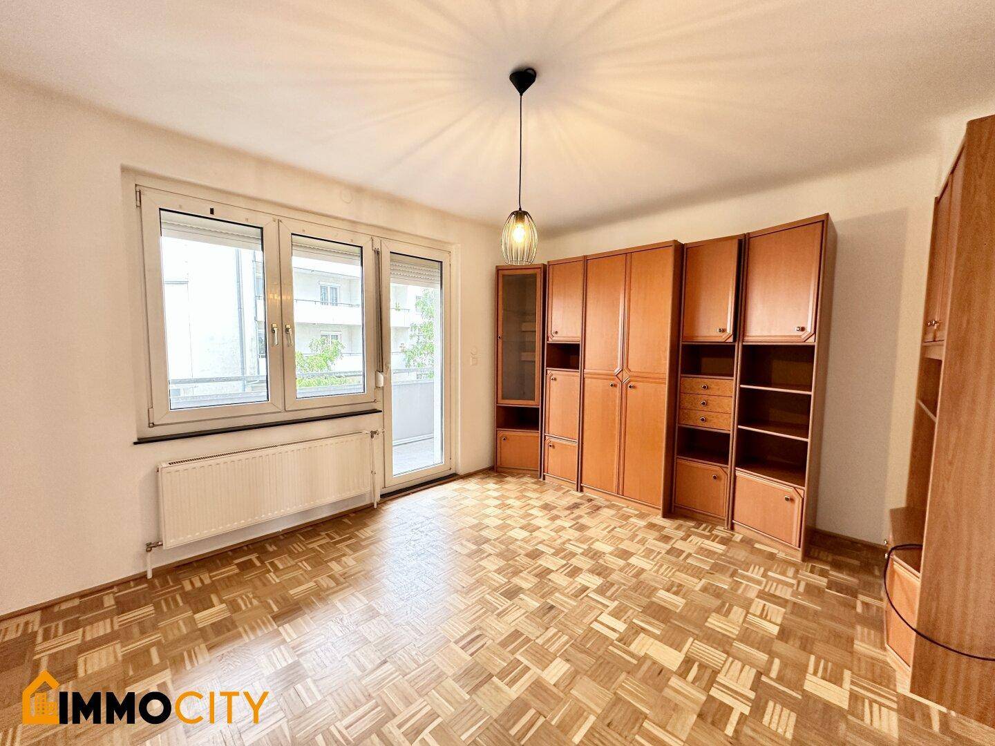 Geräumiges Zimmer mit Parkettboden, großen Schränken und Zugang zu einem Balkon.