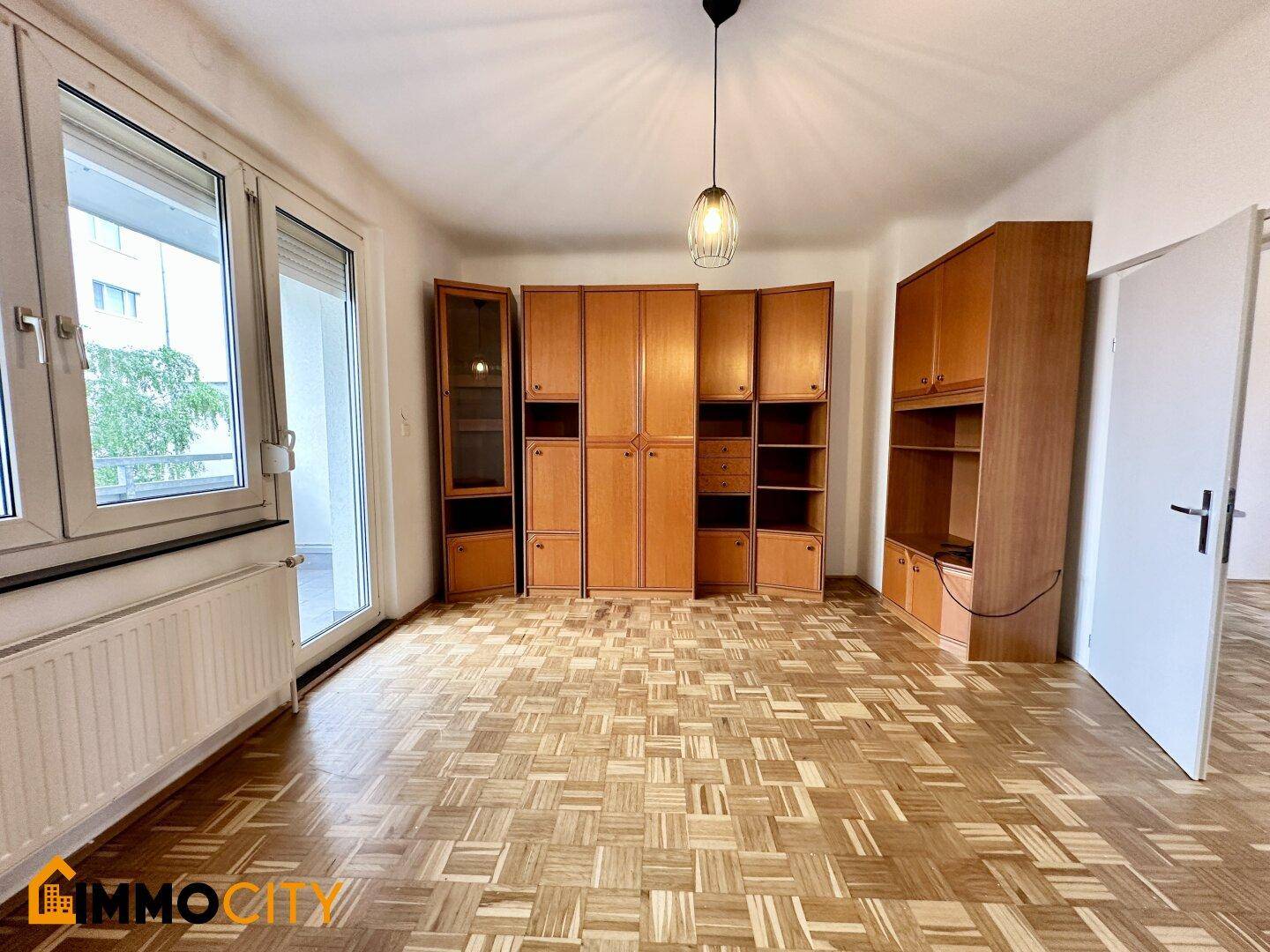 Geräumiges Zimmer mit Parkettboden, großen Schränken und Zugang zu einem Balkon.