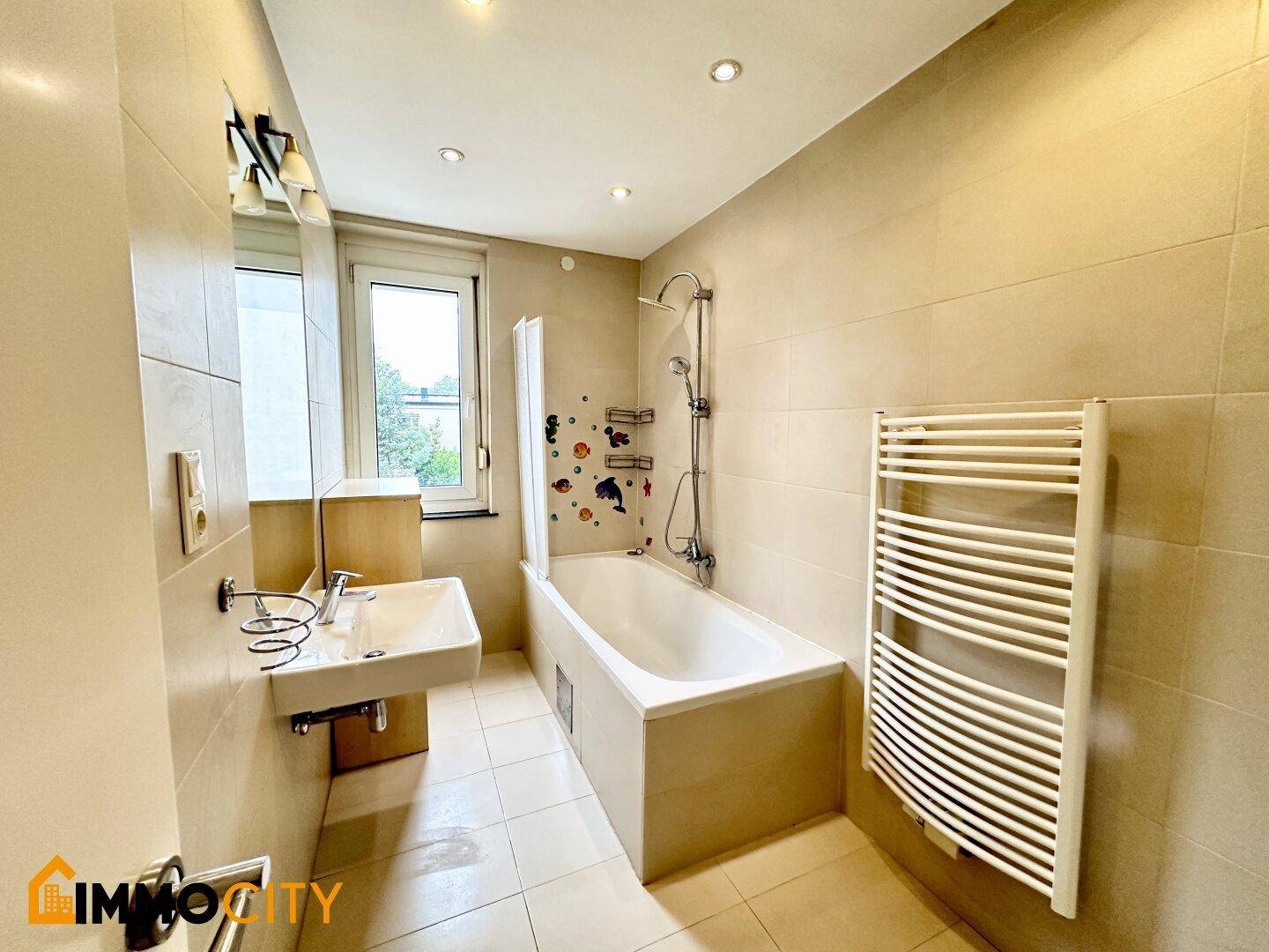 Badezimmer mit Badewanne, Dusche, Waschbecken, Fenster und einem praktischen Handtuchheizkörper.