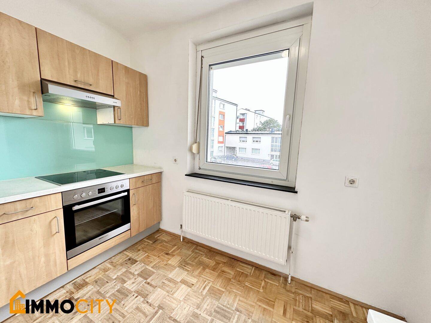 Funktionale Küche mit Holzschränken, Kochfeld, Backofen und einem Fenster für Tageslicht.