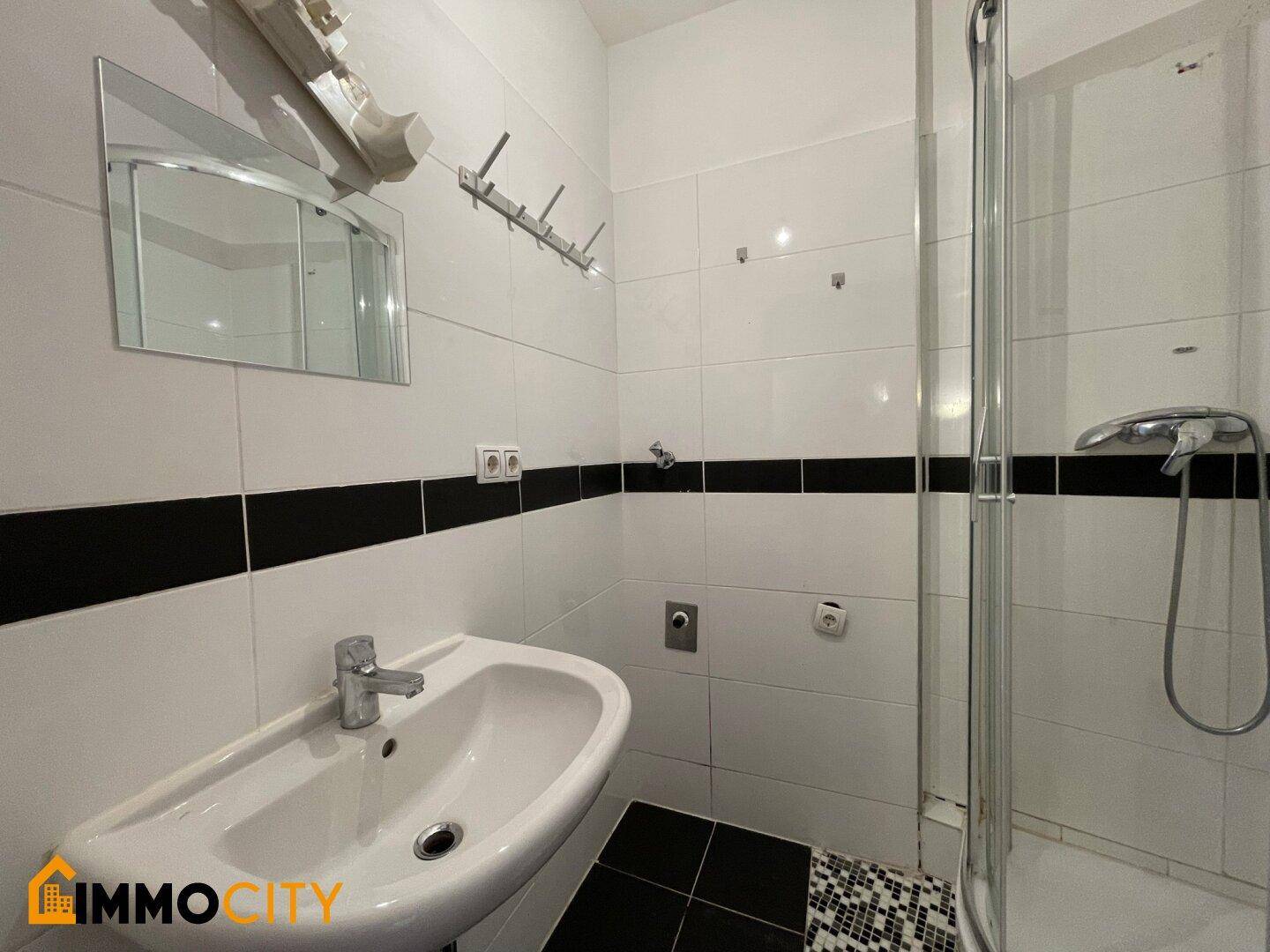 Funktionales Badezimmer mit Duschkabine, Waschbecken und sauberer Fliesenverkleidung.