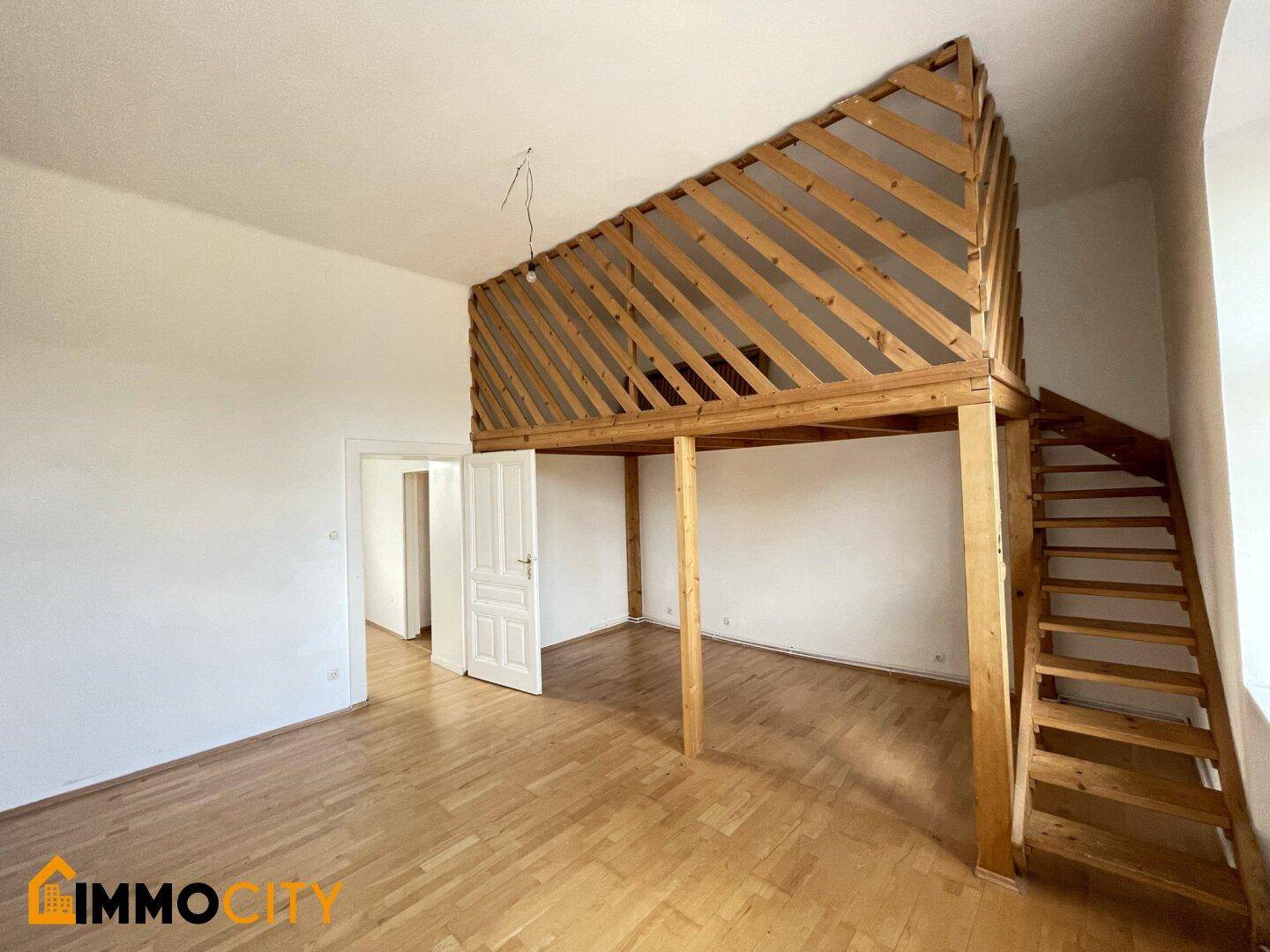 Heller Raum mit einer markanten Holzgalerie und Zugang zu weiteren Zimmern.