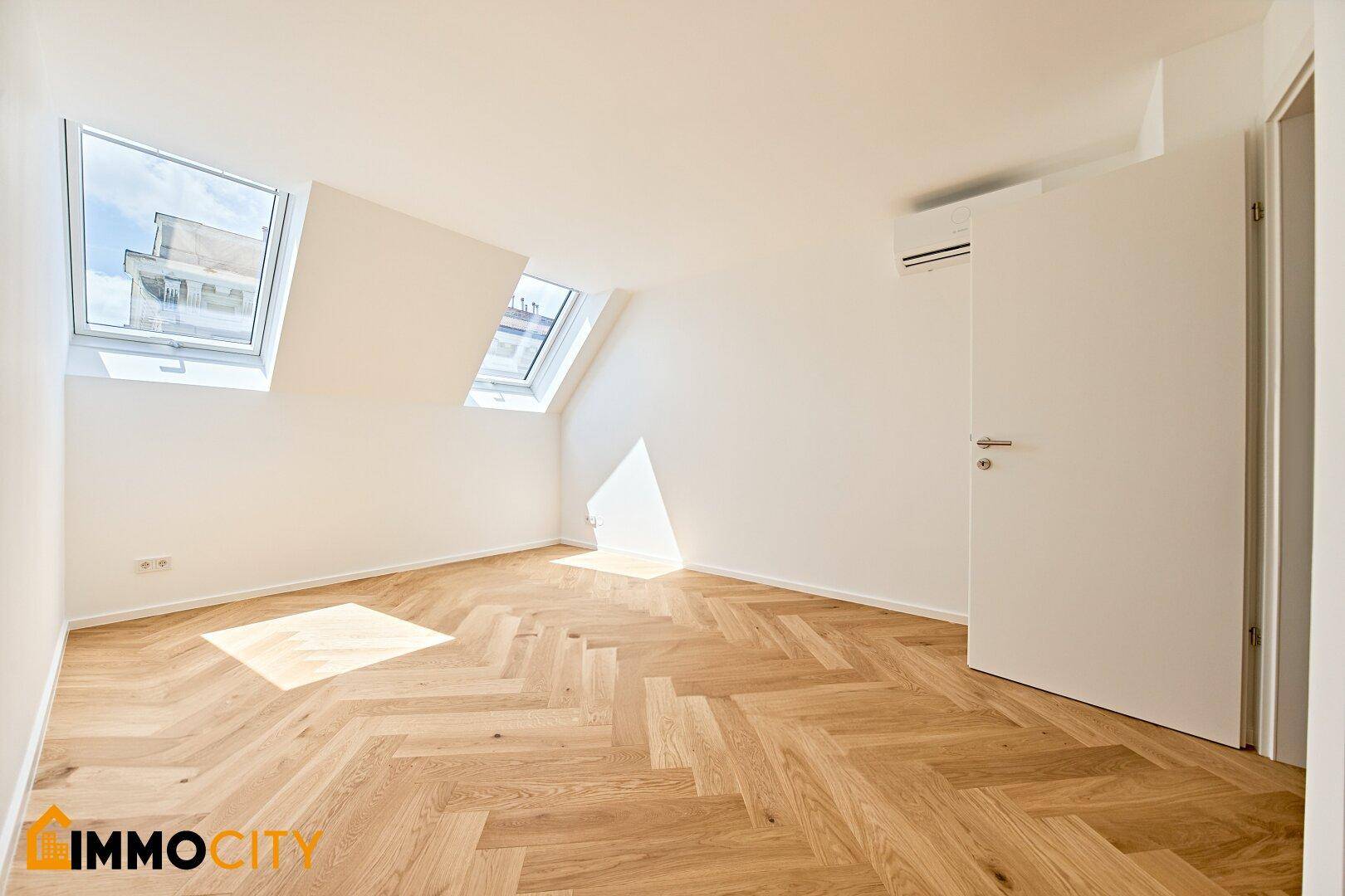 Helles Schlafzimmer mit Dachschrägen, Fischgrätparkett, Dachfenstern und Klimaanlage.