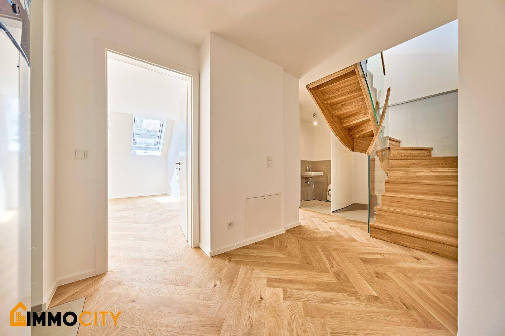 Flur mit Fischgrätparkett, Treppe und Blick in ein angrenzendes Zimmer mit Dachfenster.