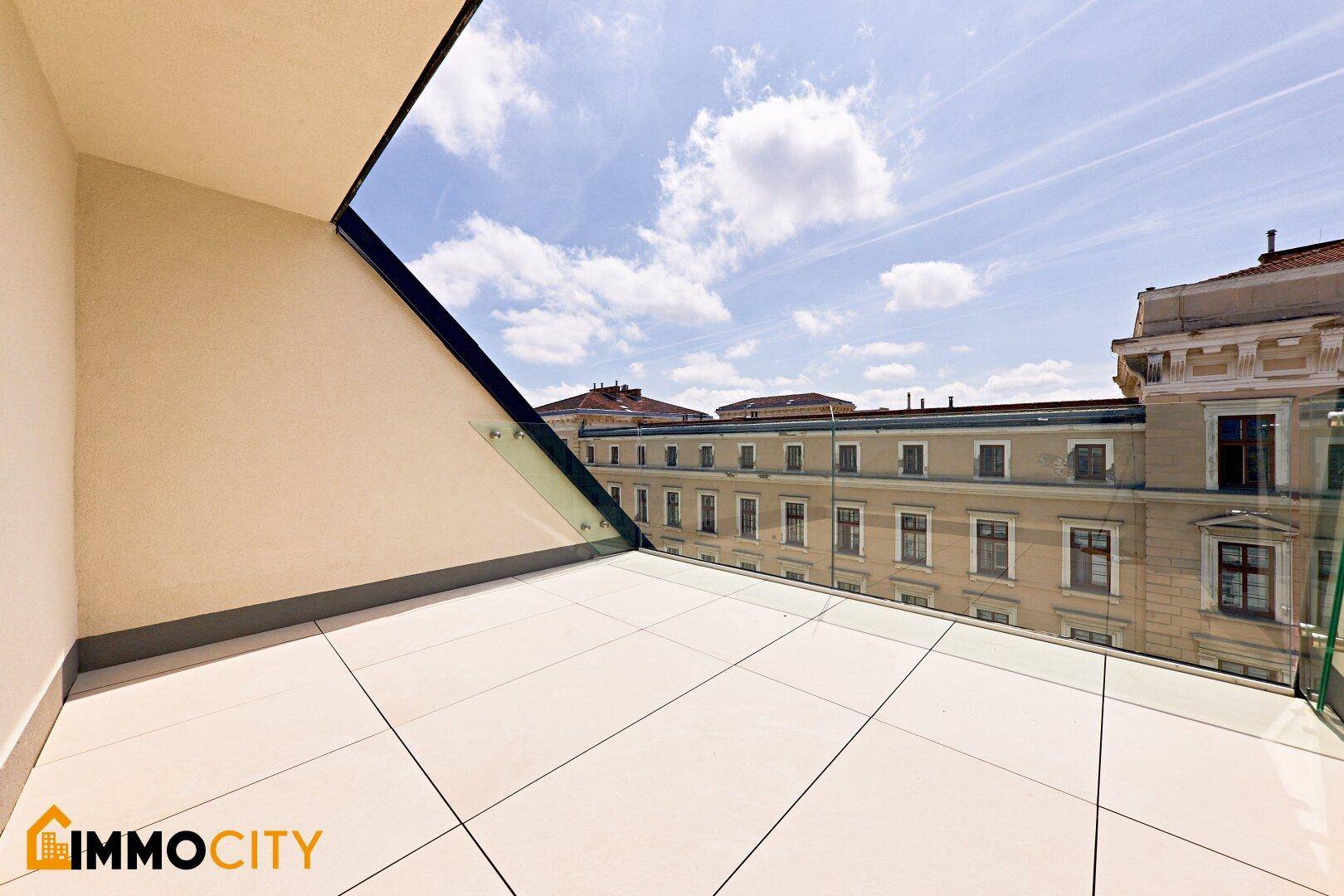 Moderne Terrasse mit Fliesenboden und Glasgeländer, bietet einen Blick auf die umliegenden Gebäude.