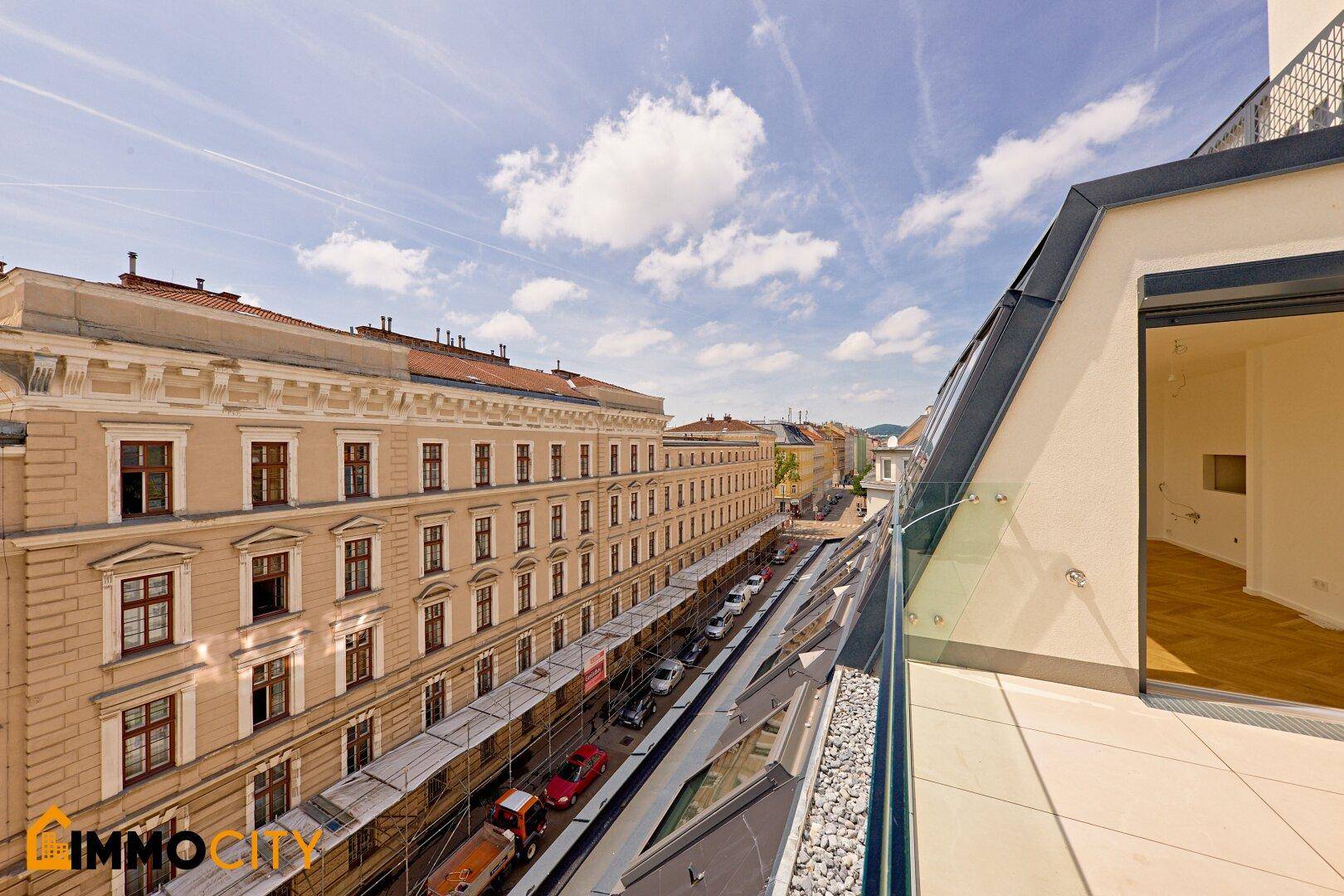 Schmaler Außenbereich mit Glasgeländer und Blick auf die Straße und historische Gebäude.