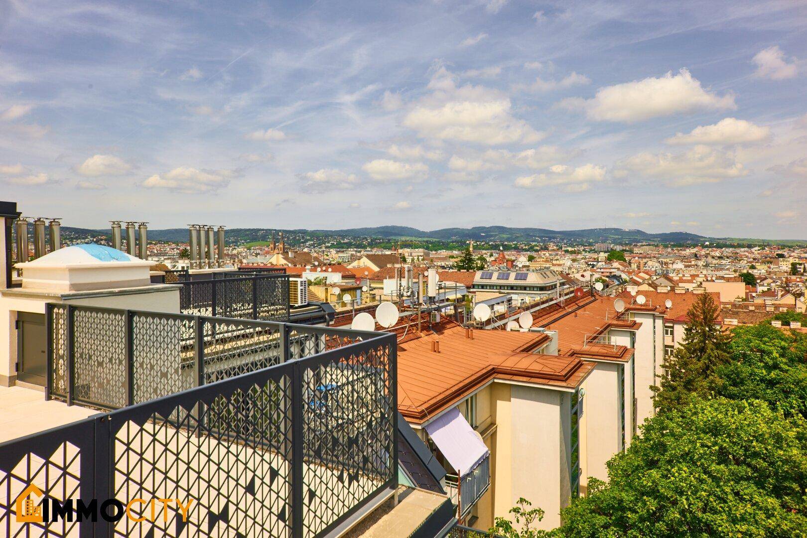 Weitläufiger Blick über die Stadt mit vielen Dächern und Bergen im Hintergrund.