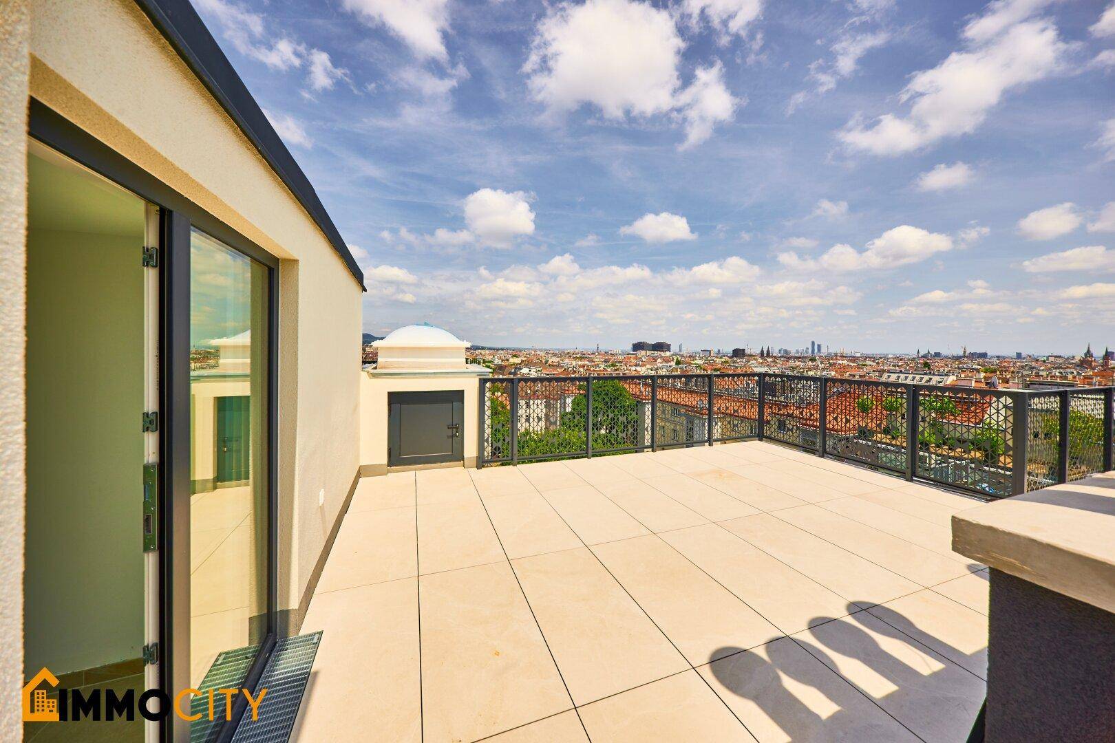Geräumige Dachterrasse mit weitem Stadtblick und moderner Brüstung unter blauem Himmel.
