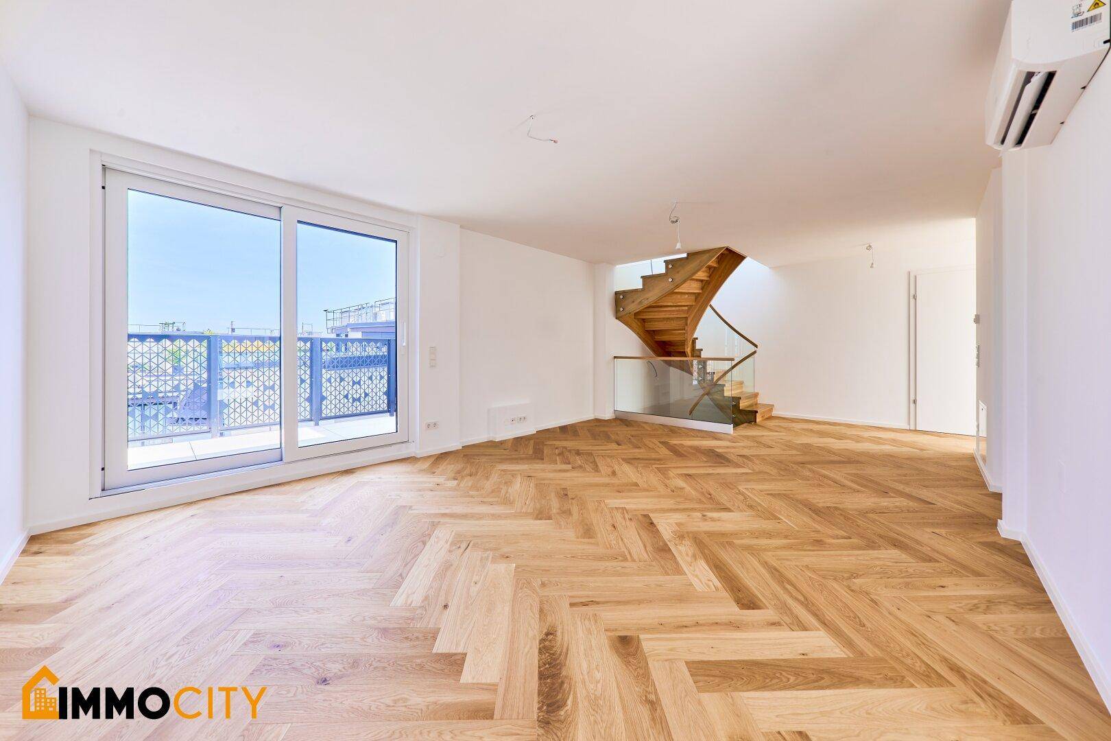 Geräumiger Wohnbereich mit Fischgrätparkett, Balkonzugang und eleganter Holztreppe.
