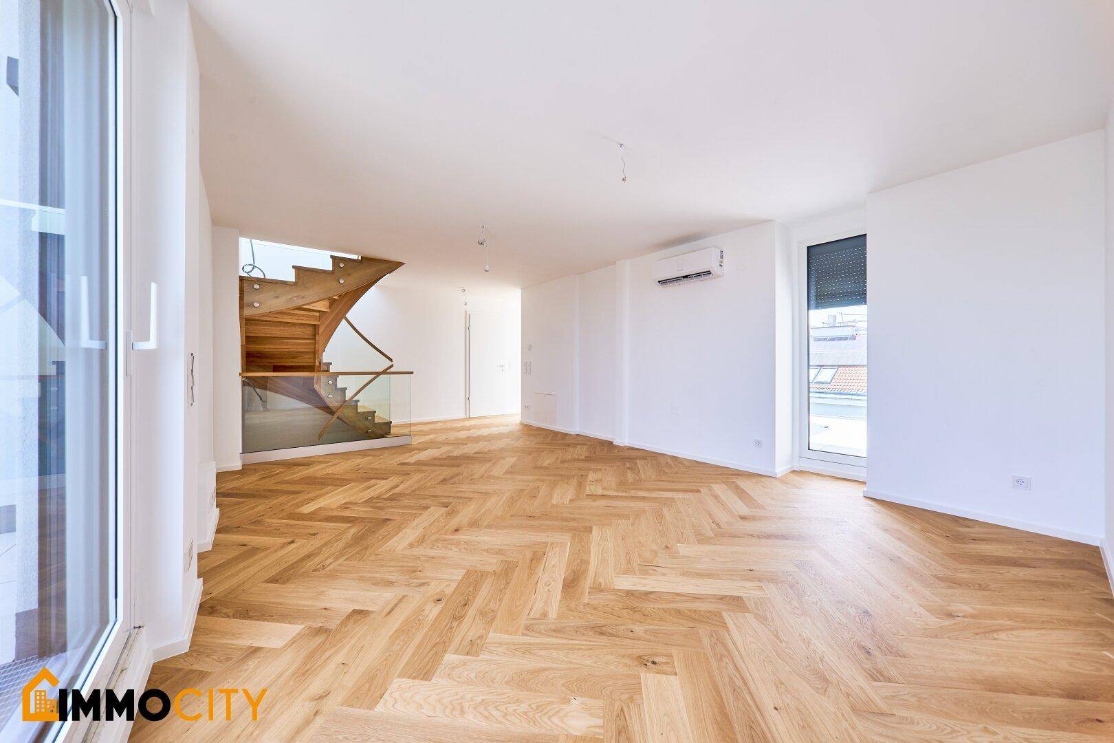 Geräumiger Wohnbereich mit elegantem Fischgrätparkett, moderner Holztreppe und Klimaanlage.