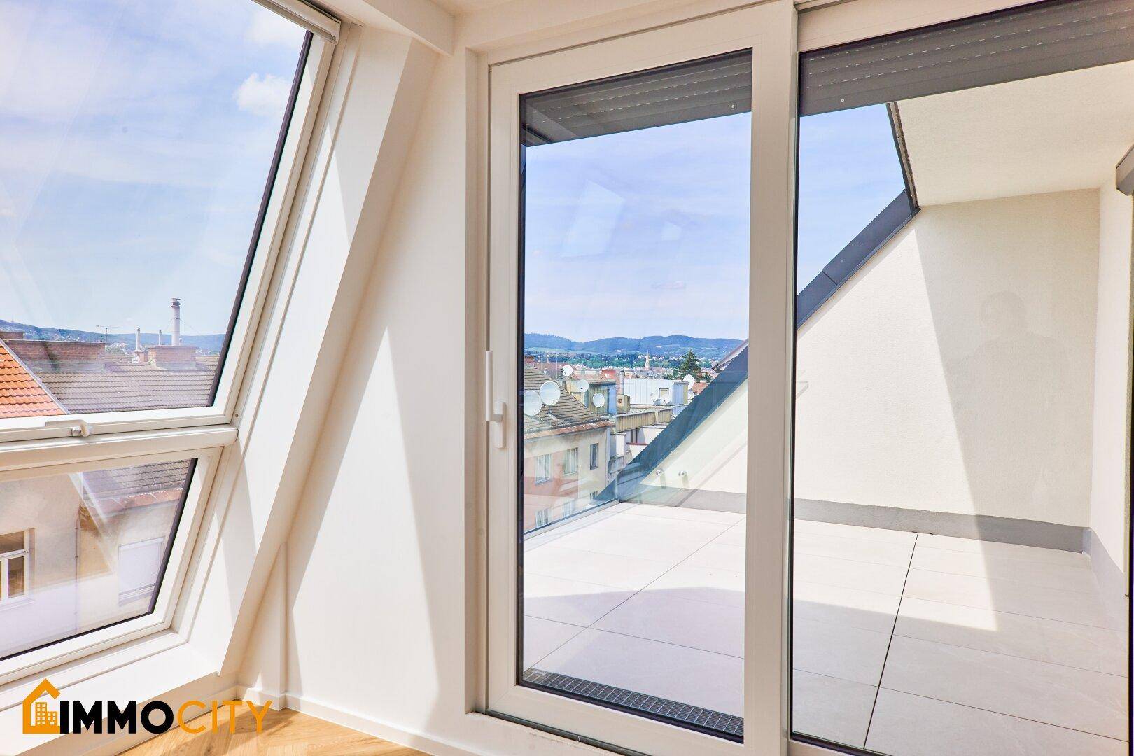 Große Glasschiebetür in einem hellen Raum, die den Blick auf die Stadt freigibt.