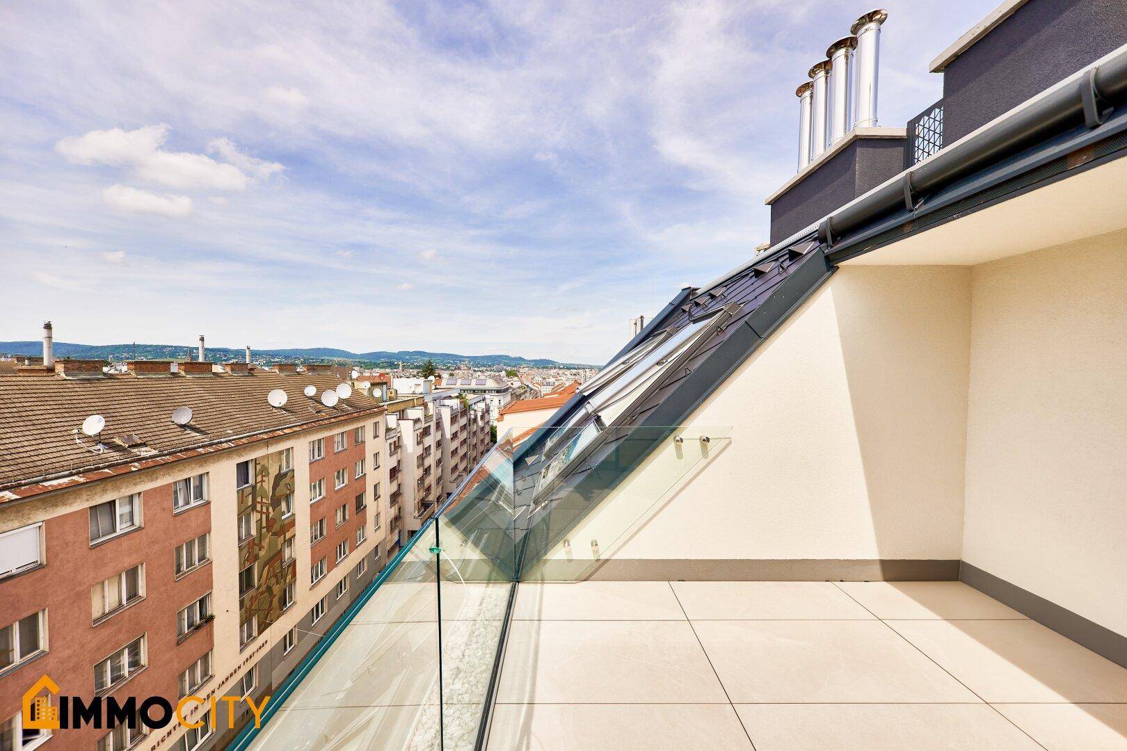 Moderner Balkon mit Glasgeländer und weitem Blick über die Stadtlandschaft und die Dächer.