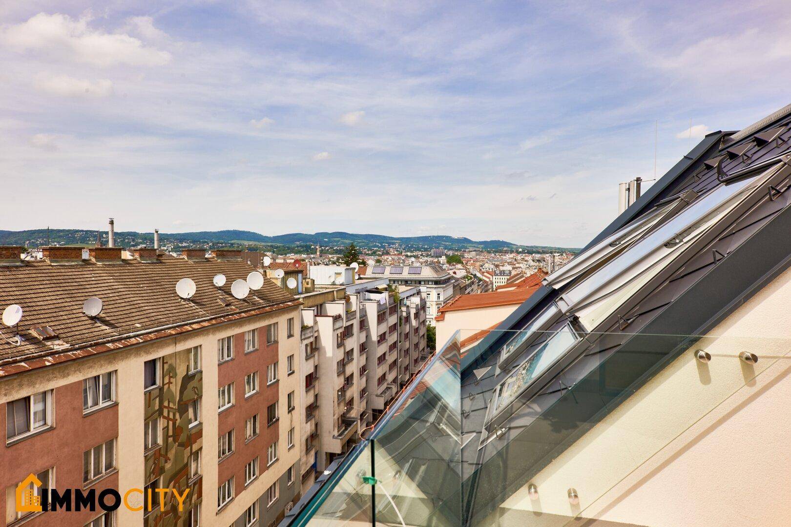 Balkon mit Glasgeländer und Panoramablick über die Stadt, inklusive Dächern und Horizont.